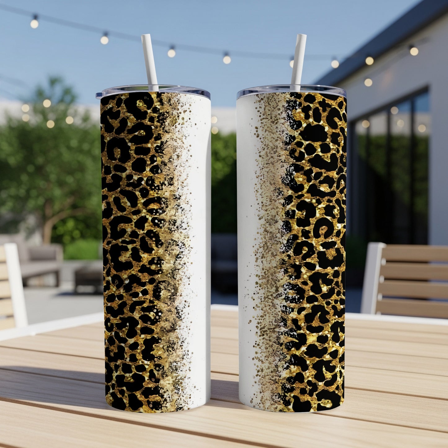 Two leopard print tumblers with straws on a table outdoors.