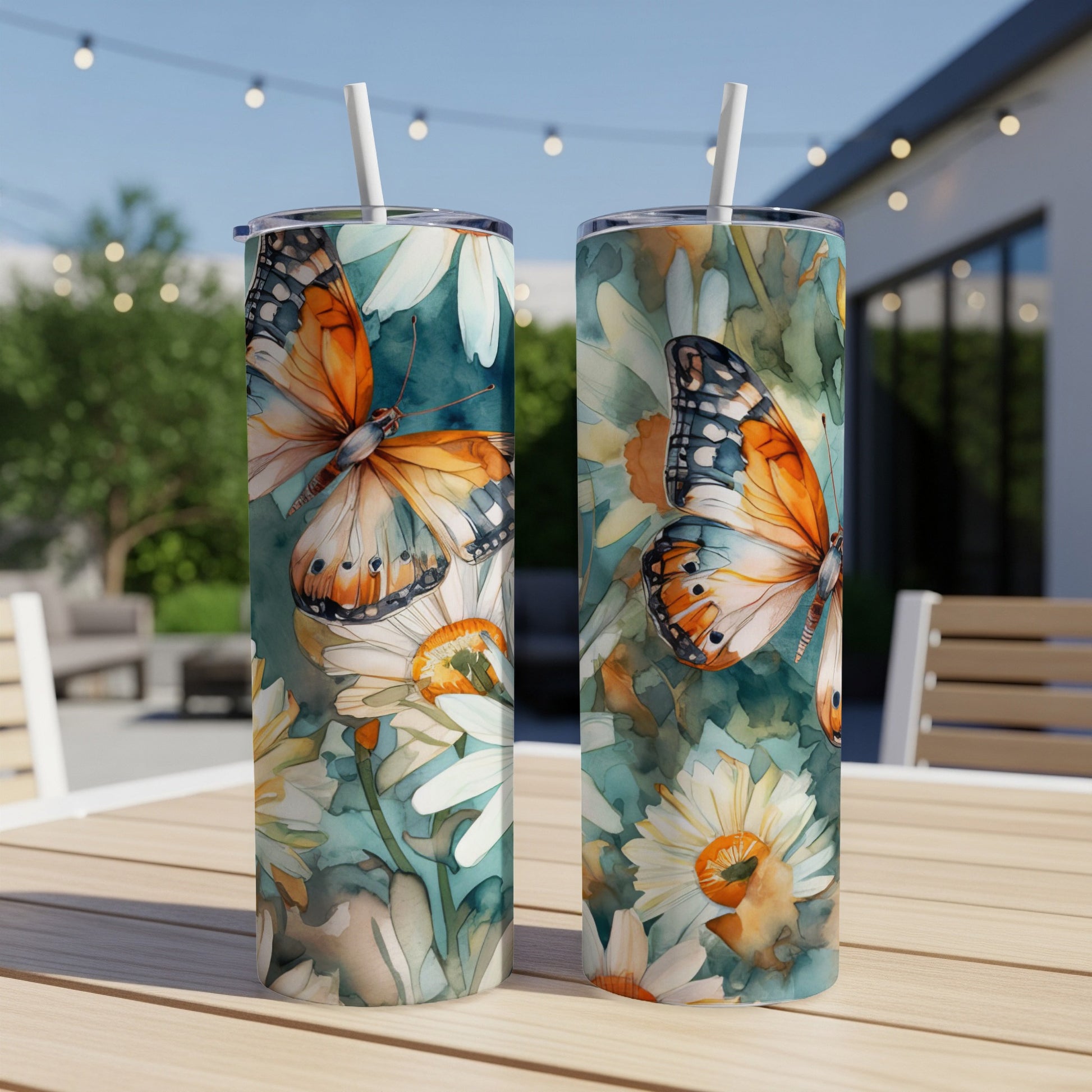 Two tumblers with monarch butterflies and daisies on a wooden table.