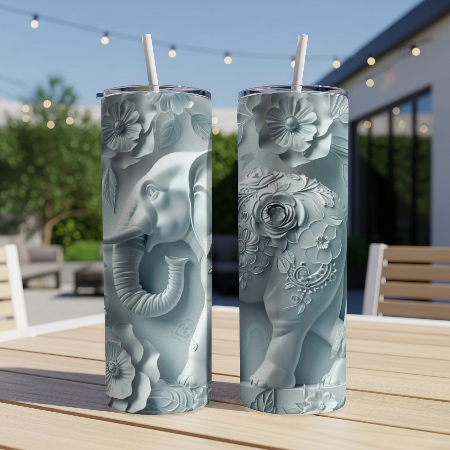 Two light blue tumblers with raised elephant and floral designs on an outdoor table.