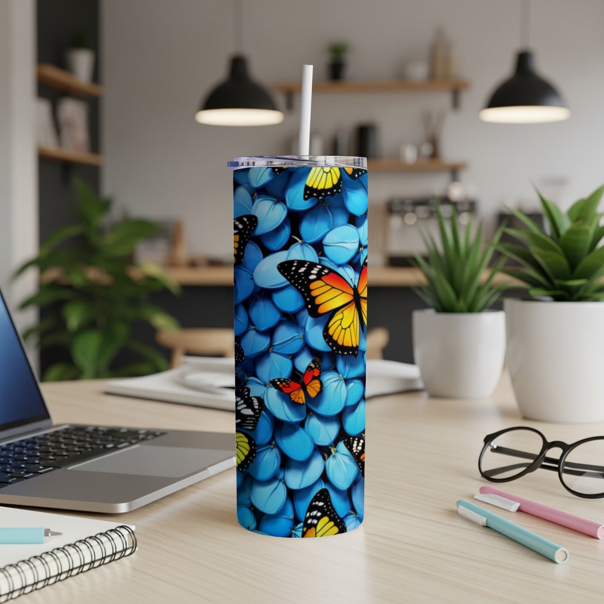 Blue tumbler with butterfly pattern on a desk with laptop.