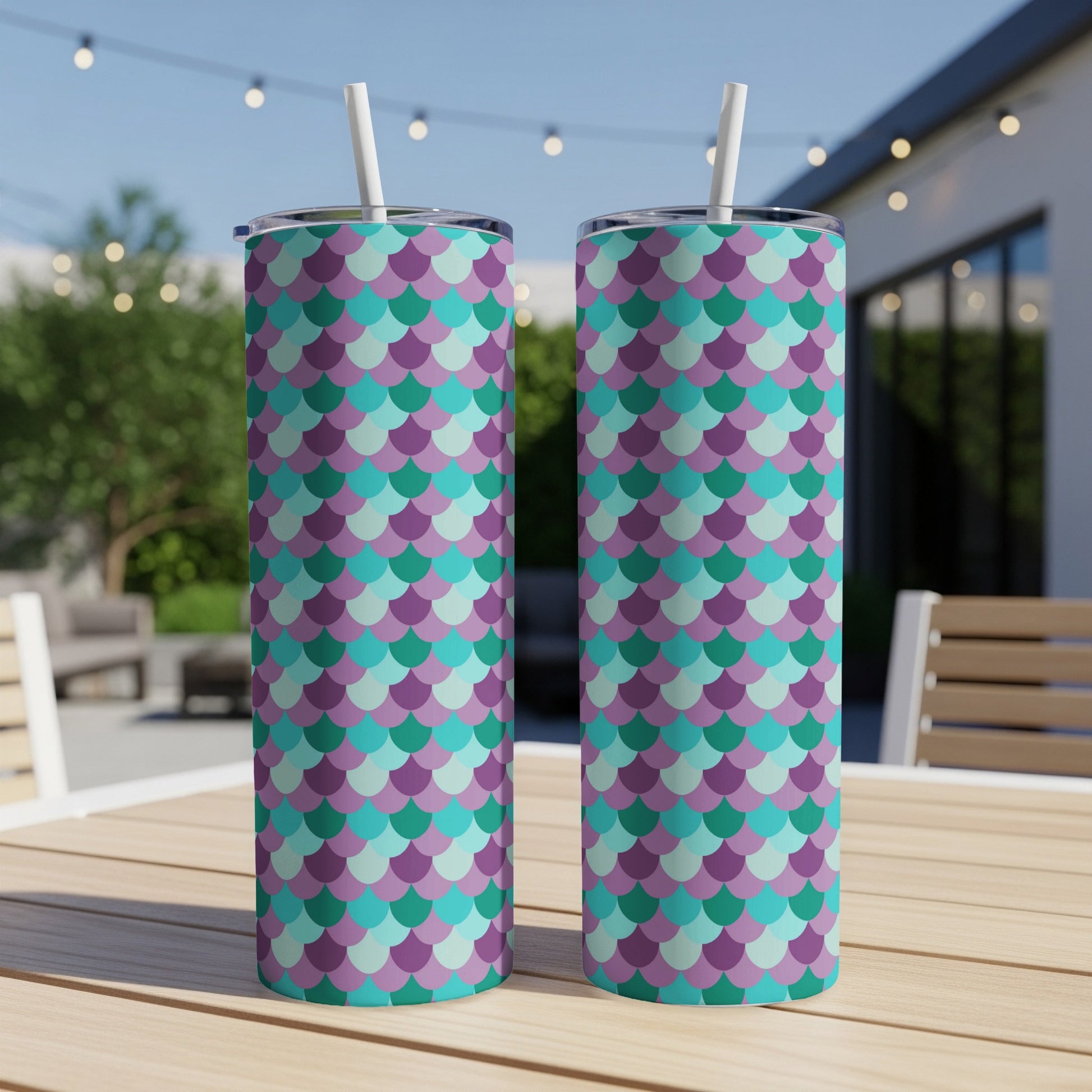 Two skinny tumblers with purple, teal, and green mermaid scale pattern and white straws.
