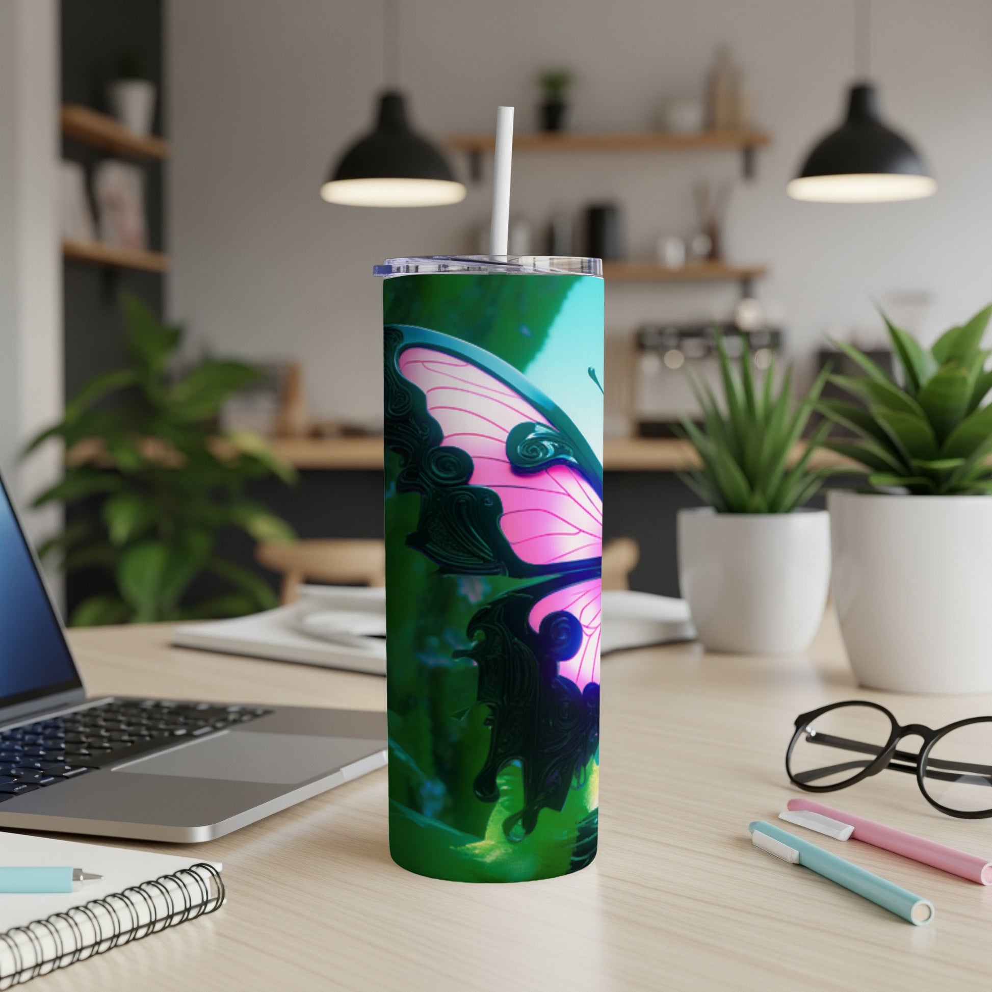 Tumbler with a pink butterfly design on a desk with a laptop and pens.