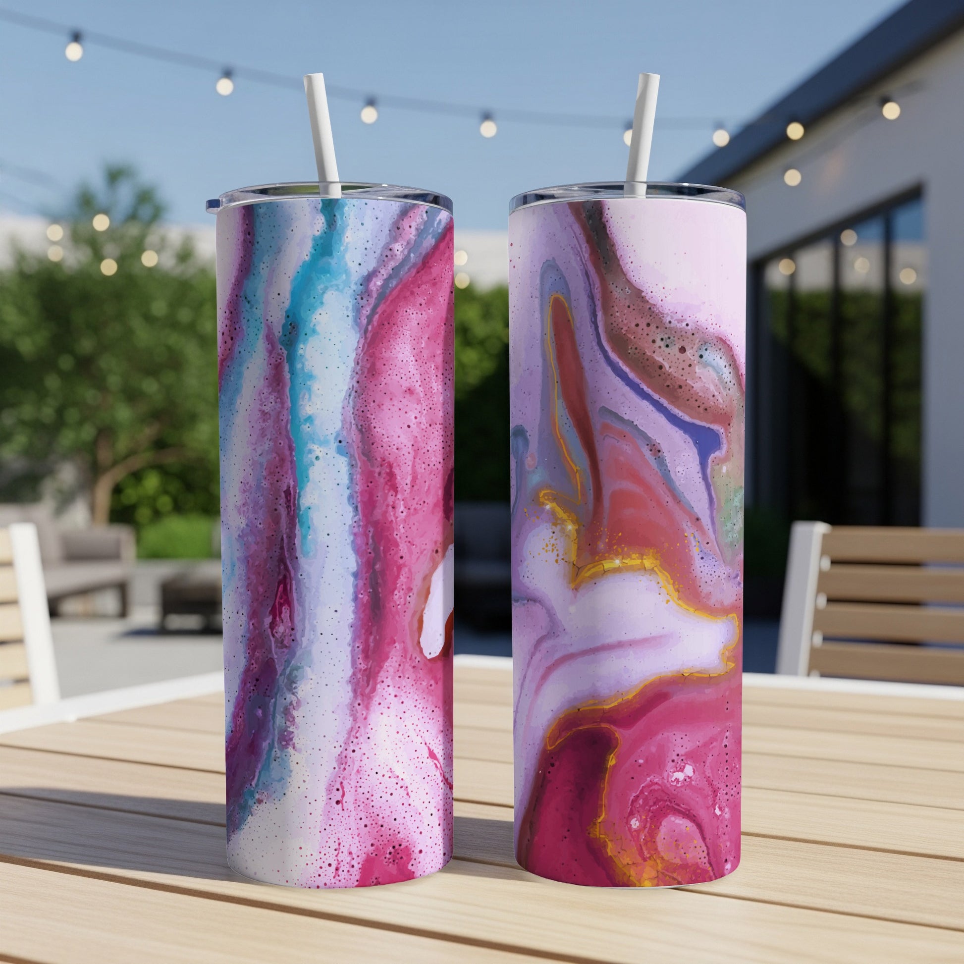 Two tumblers with colorful marbled abstract designs sit on a wooden table outdoors.