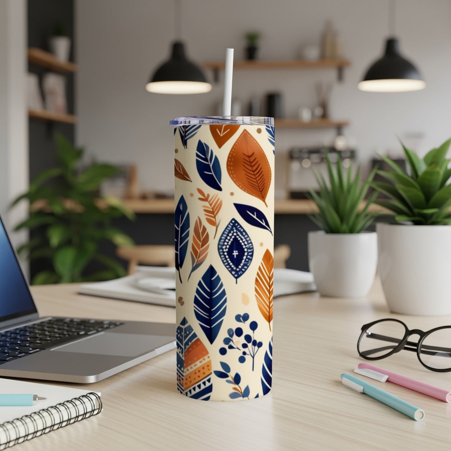 Blue and orange leaf pattern on a white skinny tumbler with a straw.