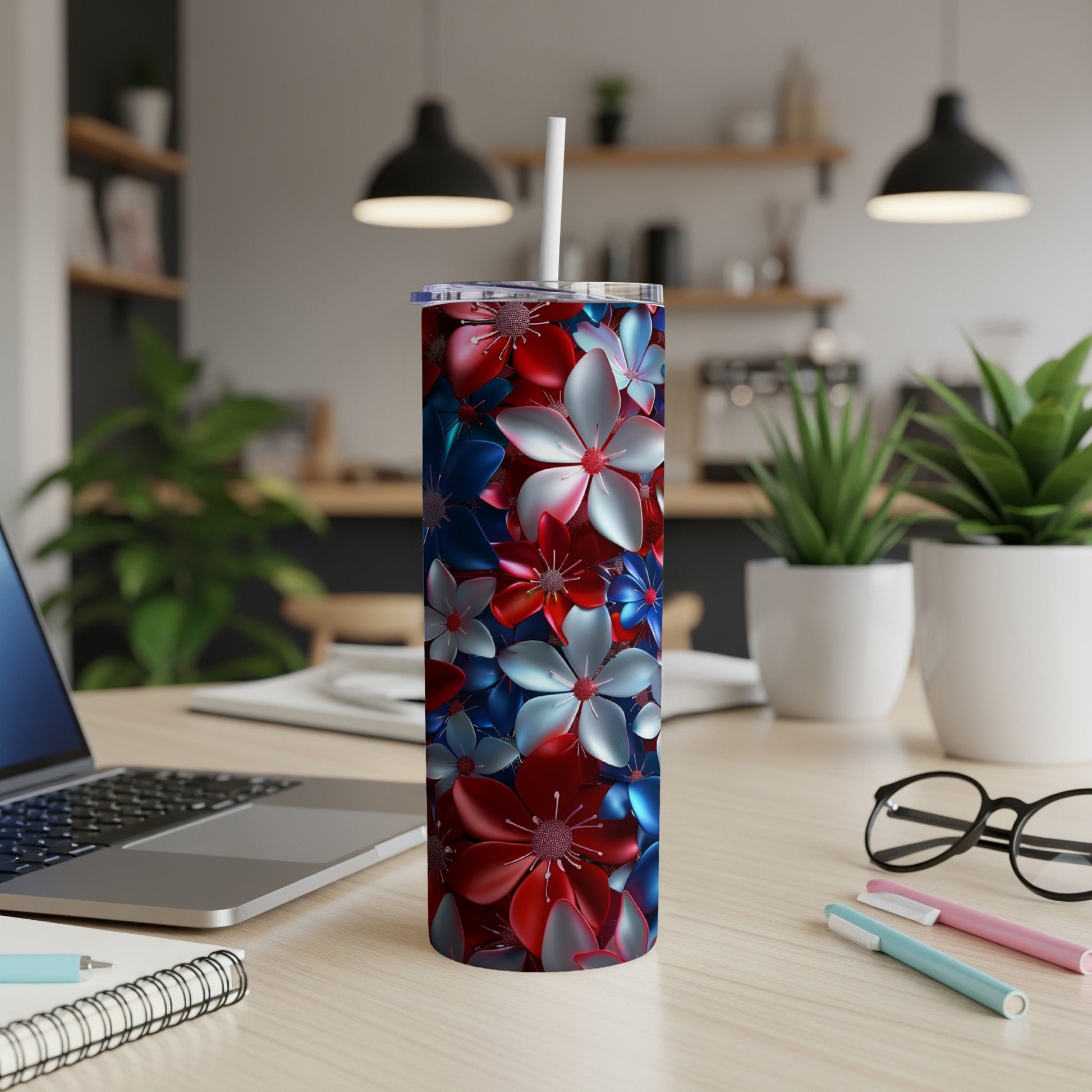 Red, white, and blue floral patterned tumbler with straw on a desk.