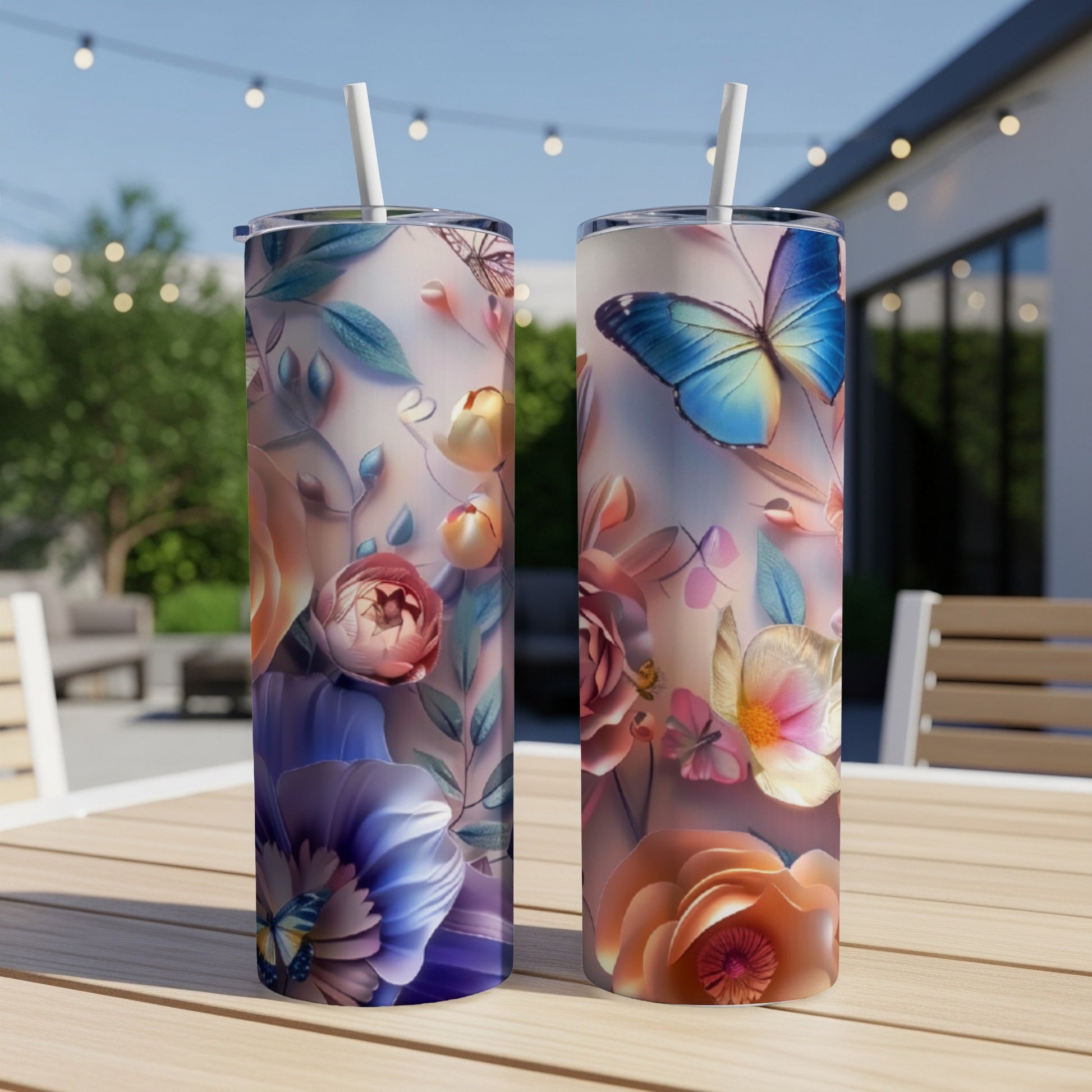 Two tall tumblers with floral and butterfly designs sit on a table outdoors.