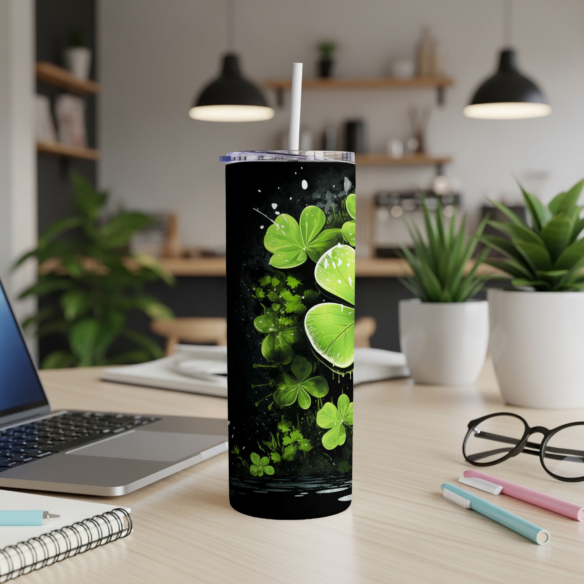 Black tumbler with green shamrocks and white splatters, on a desk.