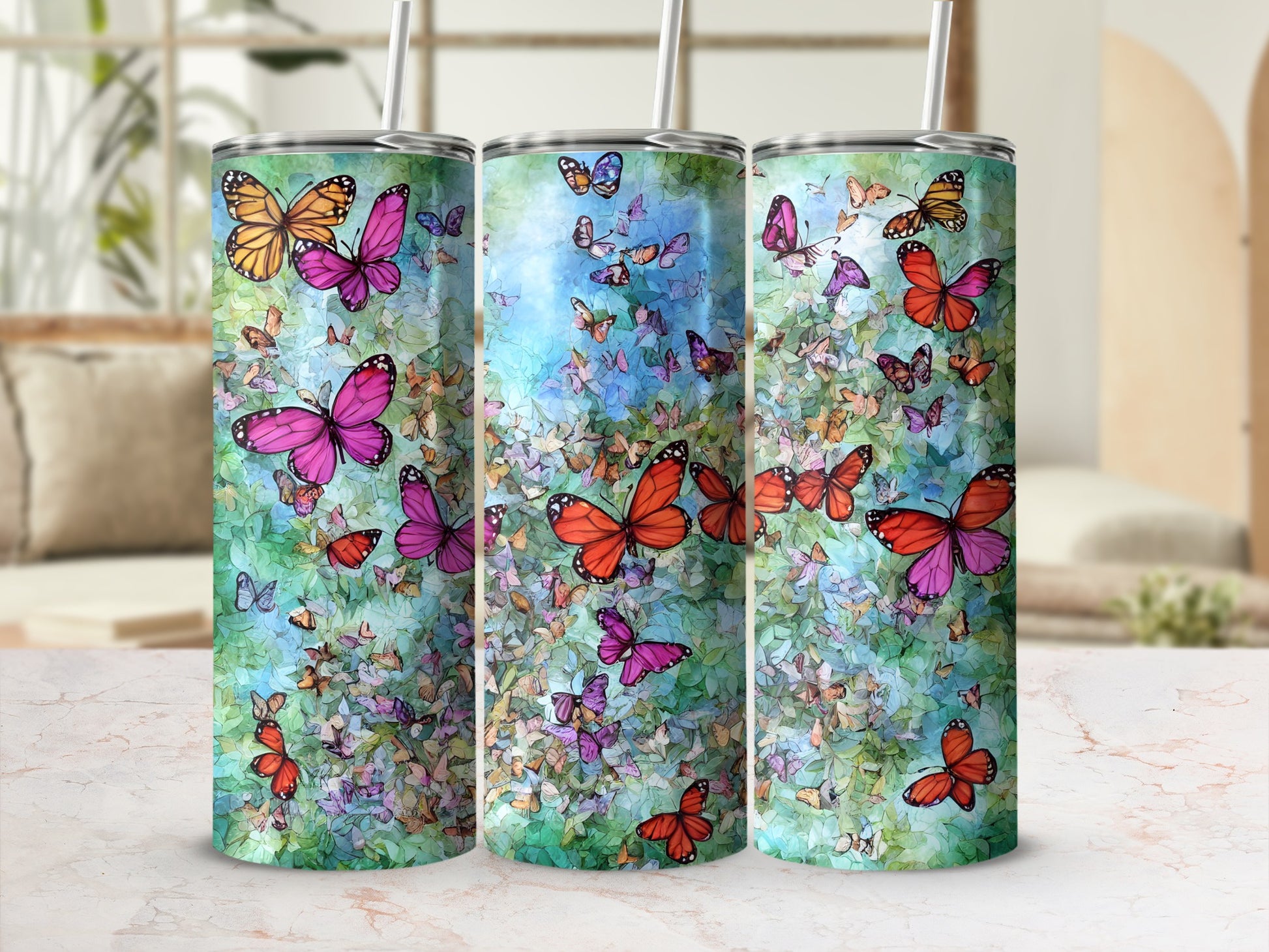Three tumblers with colorful butterflies and floral patterns on a marbled surface.