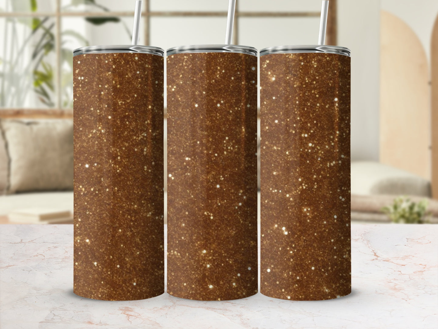 Three glittery brown tumblers with straws stand on a marbled surface.