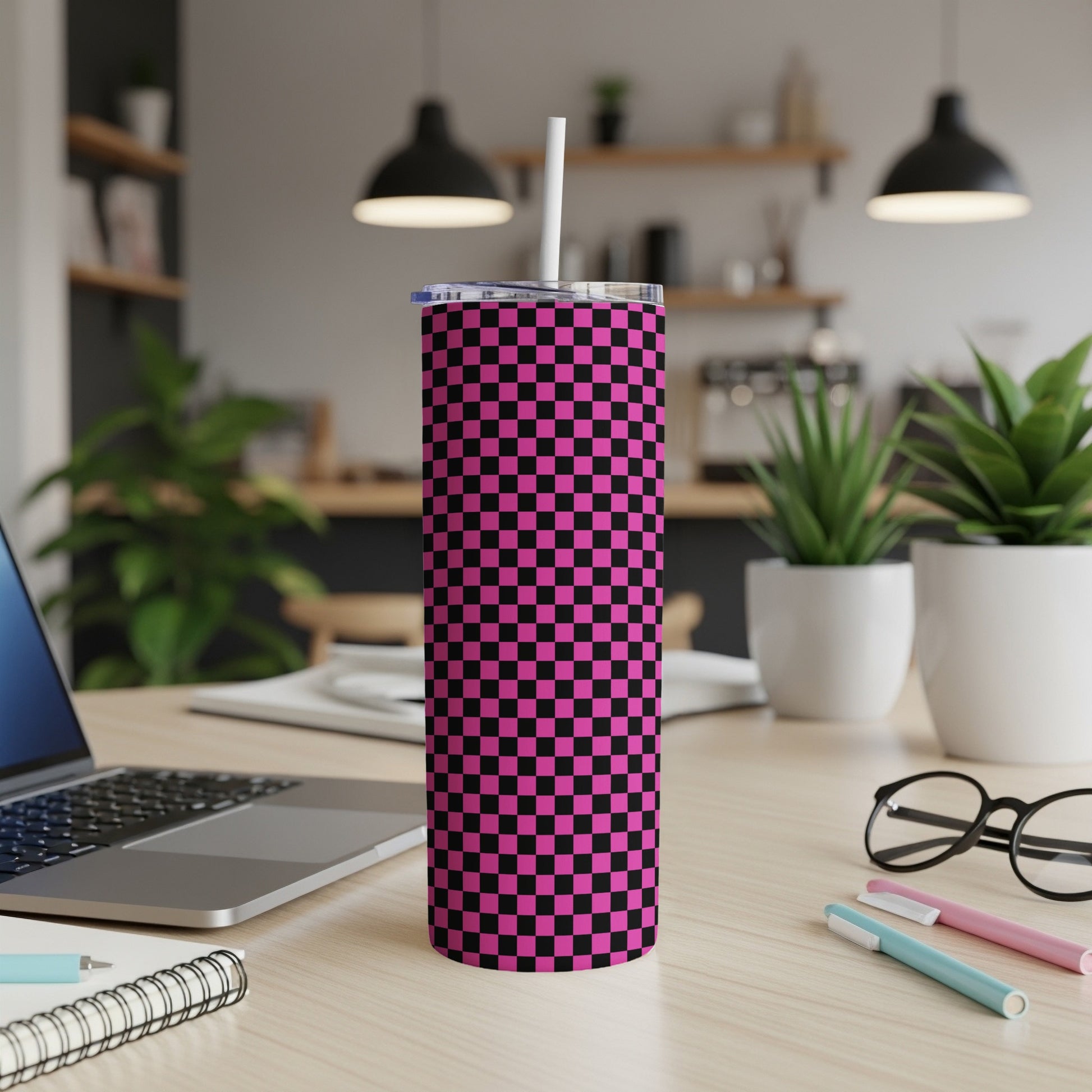 Pink and black checkered tumbler with straw on a desk.