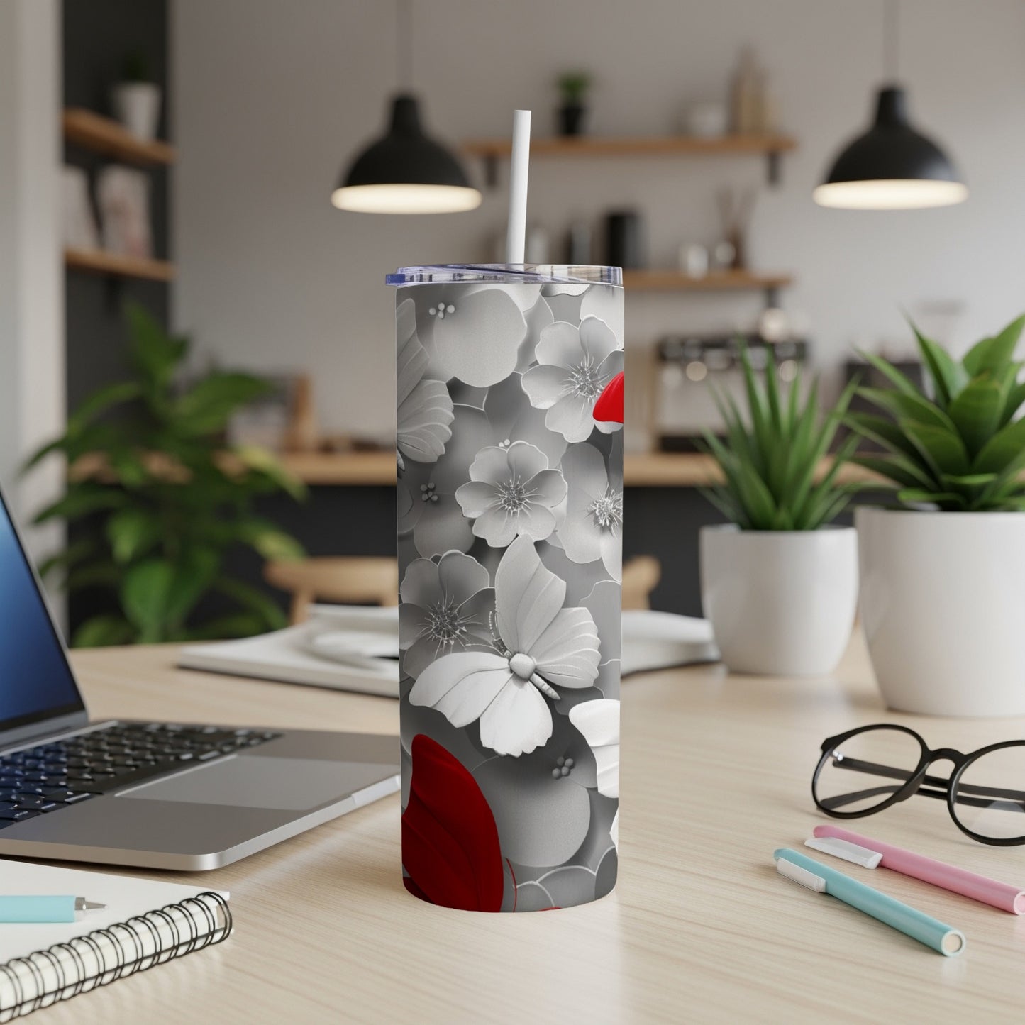 White floral tumbler with red accents and a straw, on a desk.