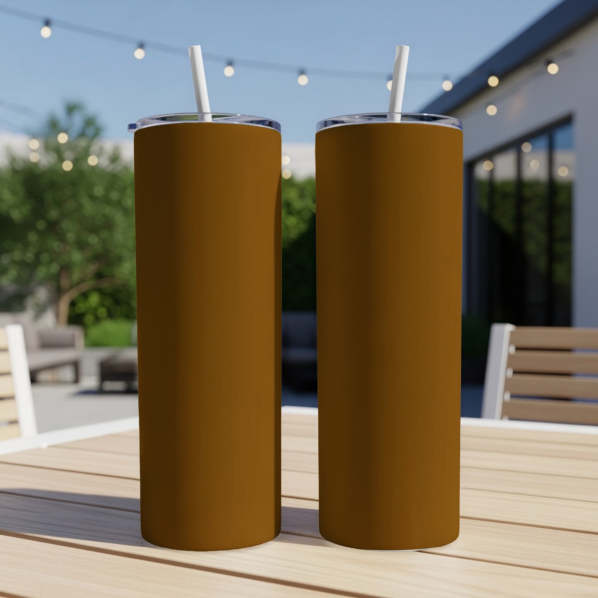 Two brown tumblers with white straws stand on a wooden table outdoors.