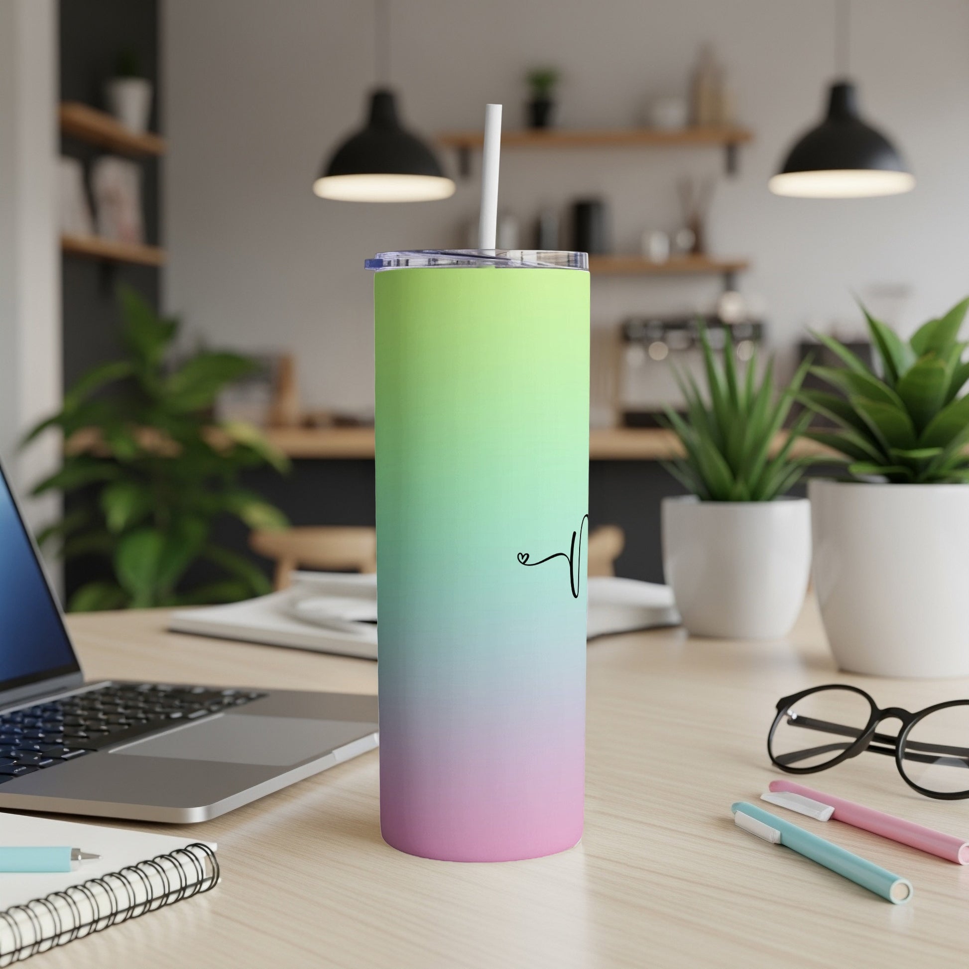 Gradient green and pink tumbler with straw on a desk.