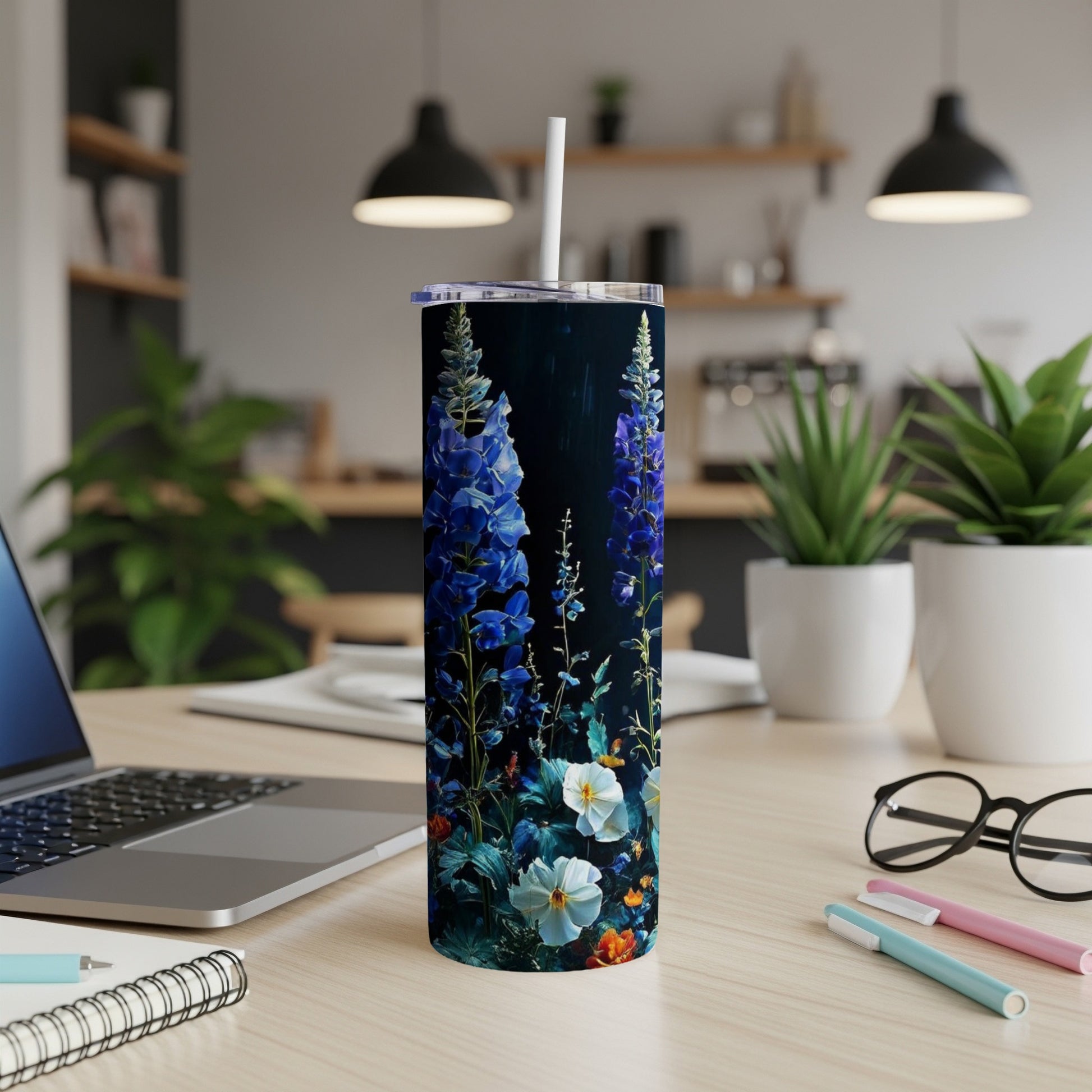 Tall tumbler with blue wildflowers and green leaves on dark background.