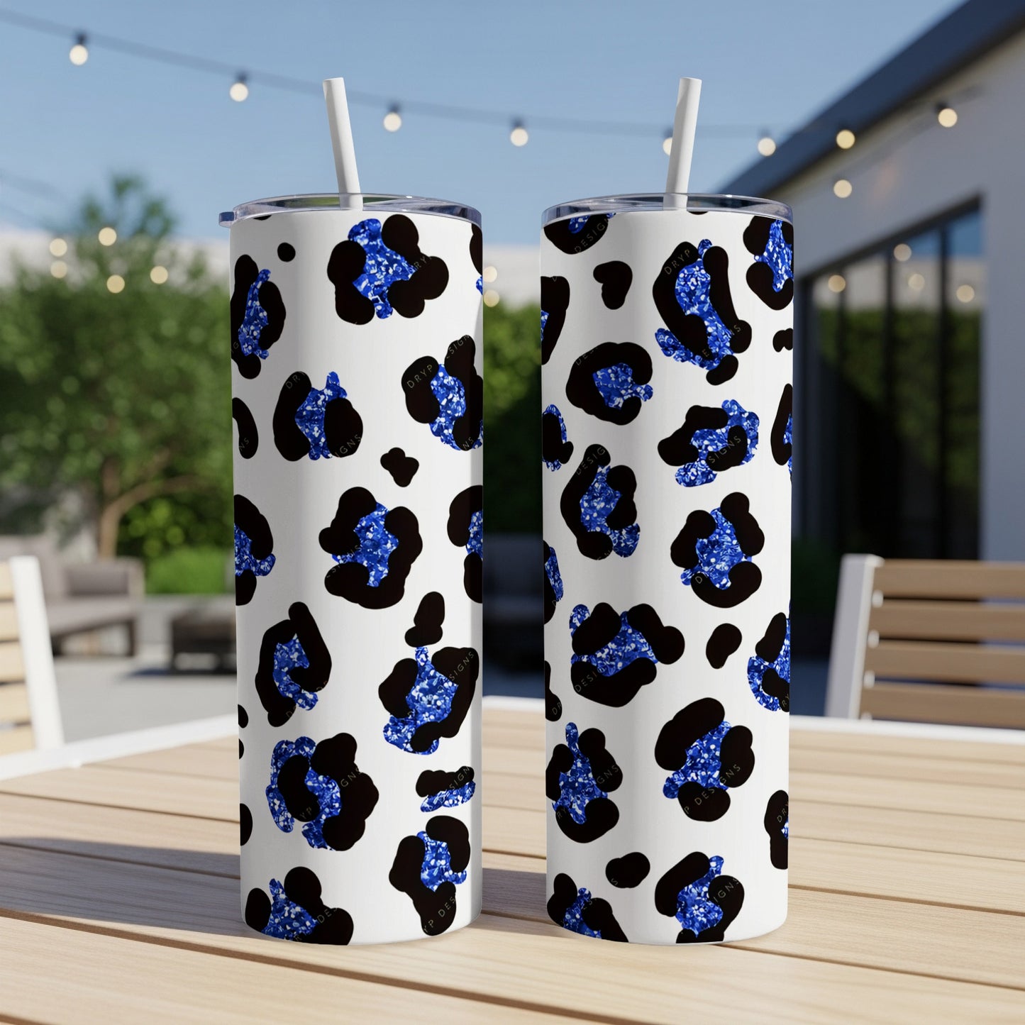 Two white tumblers with blue glitter leopard print, on a table outdoors.