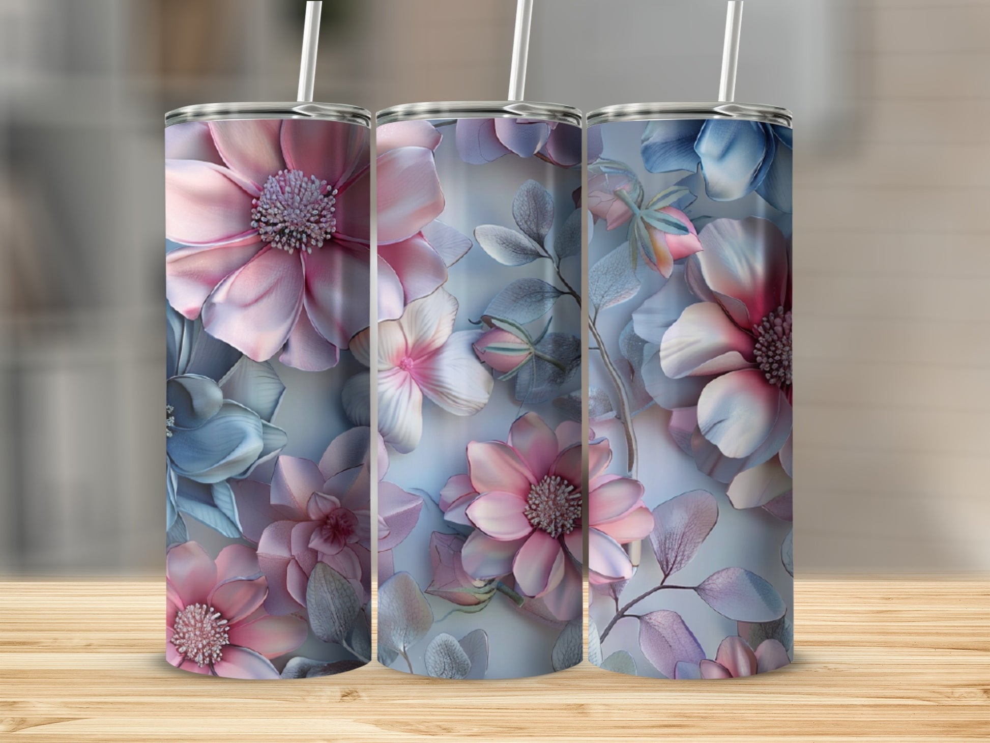 Three pink and blue floral tumblers with straws on a wooden surface.