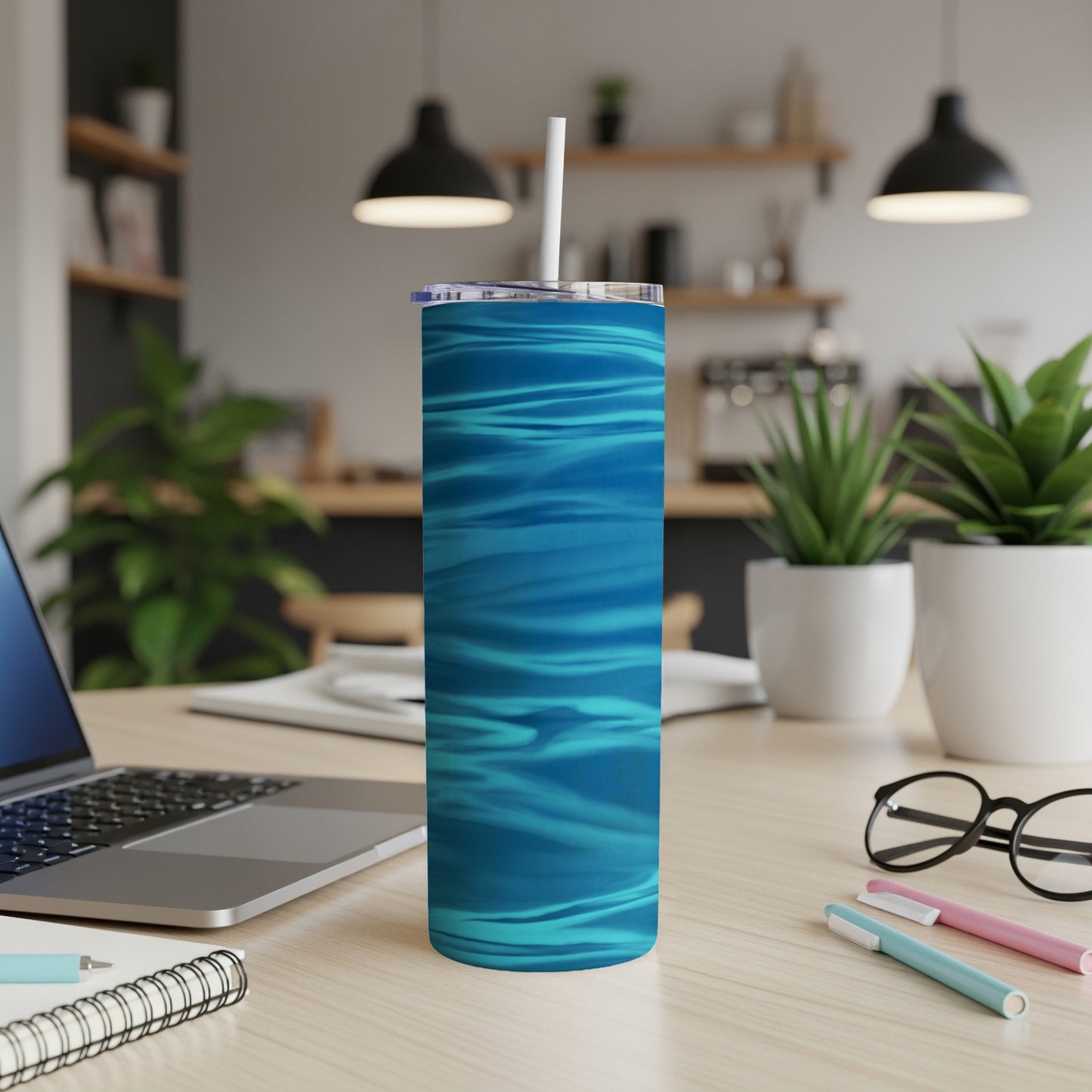 Blue striped tumbler with straw on a wooden desk with laptop and plants.