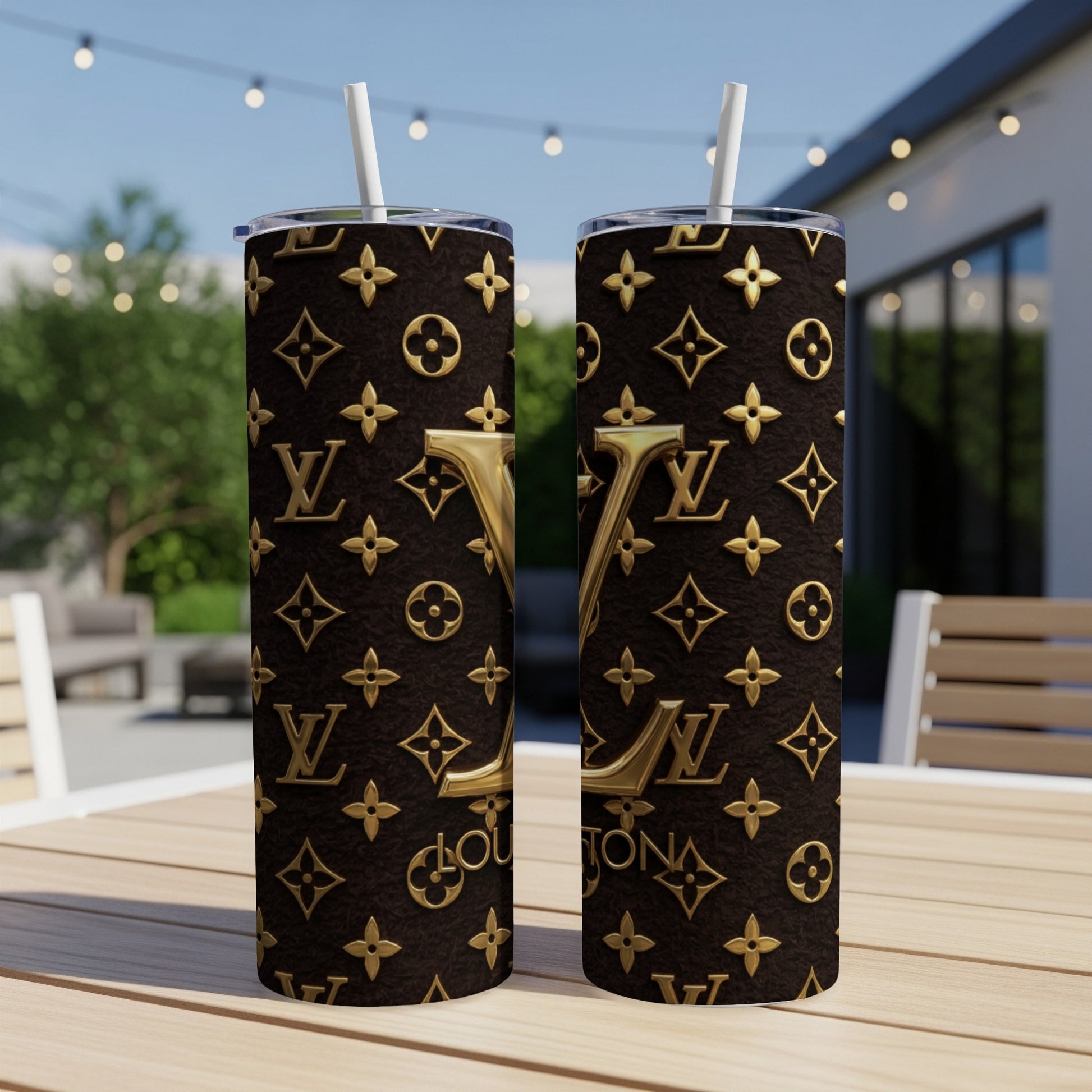 Two brown tumblers with gold LV pattern and straws on a wooden table.