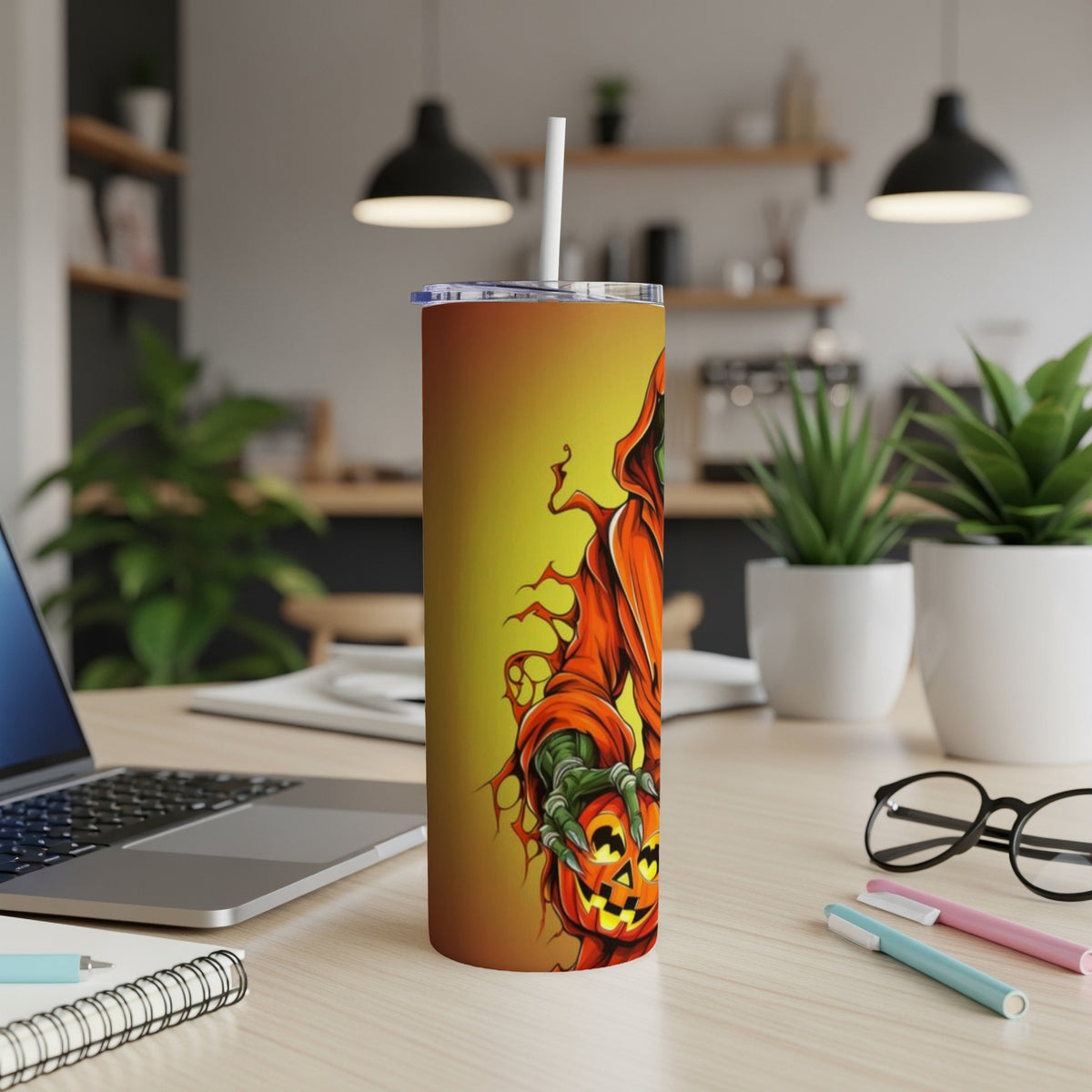 Tumbler with an orange hooded figure holding a jack-o'-lantern, on a desk.