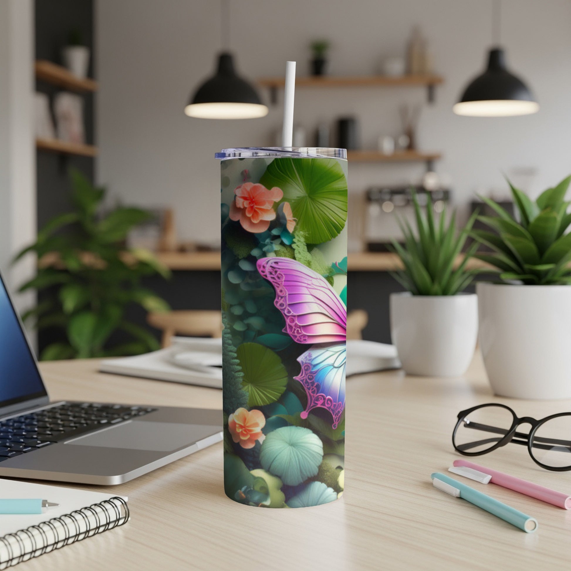Tumbler with butterfly and floral design, straw, on a desk.