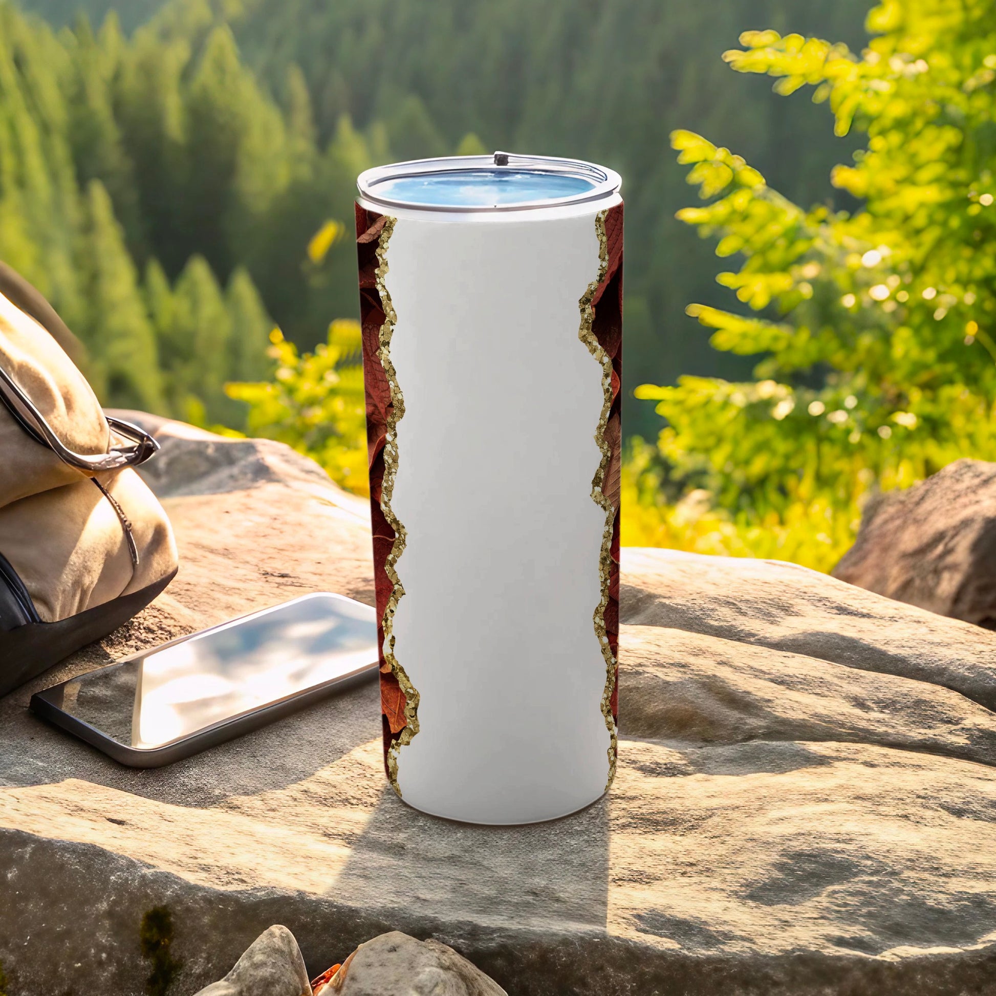 White tumbler with brown and gold leaf pattern on outdoor rock surface.