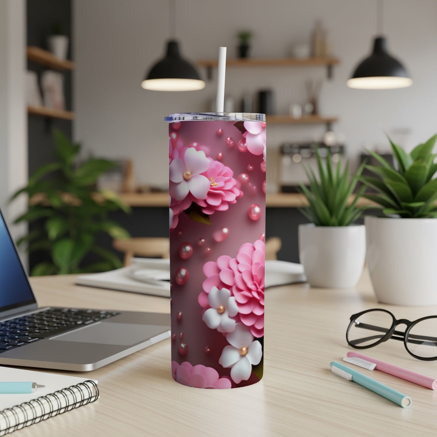 Pink floral tumbler with white straw on a desk with laptop and pens.