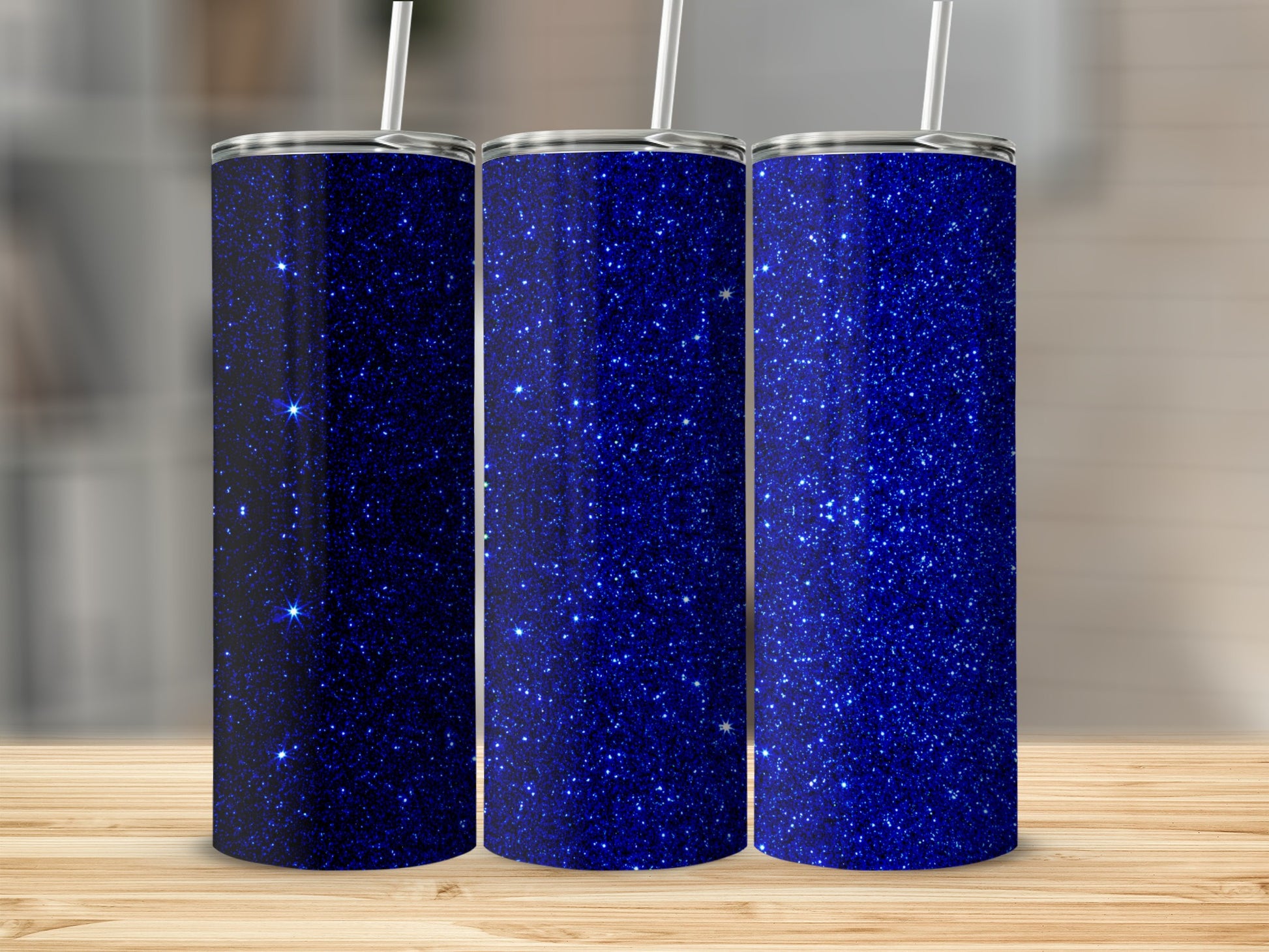 Three sparkly blue tumblers with straws displayed on a wooden surface.