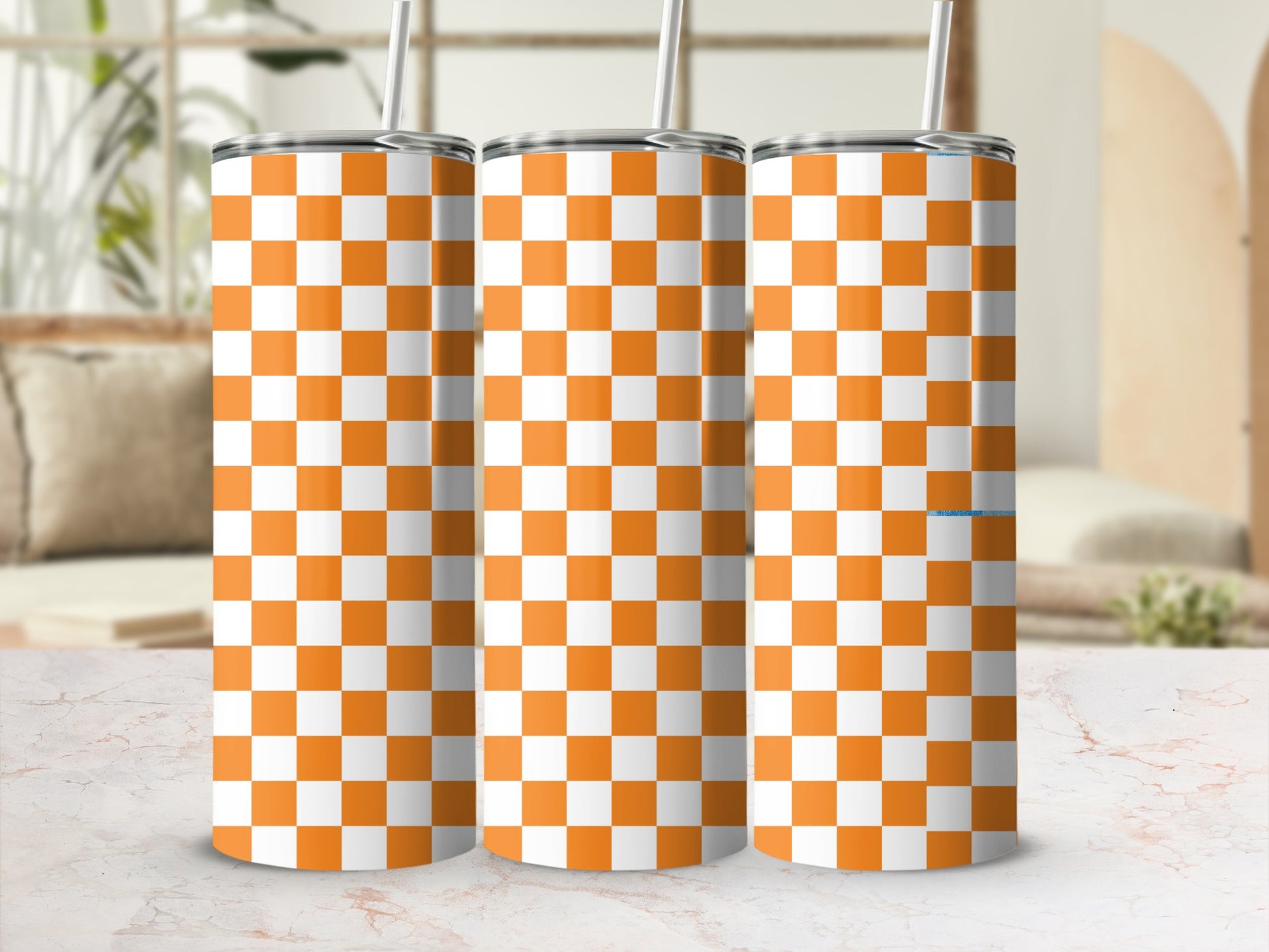 Three orange and white checkered tumblers with straws in a row.
