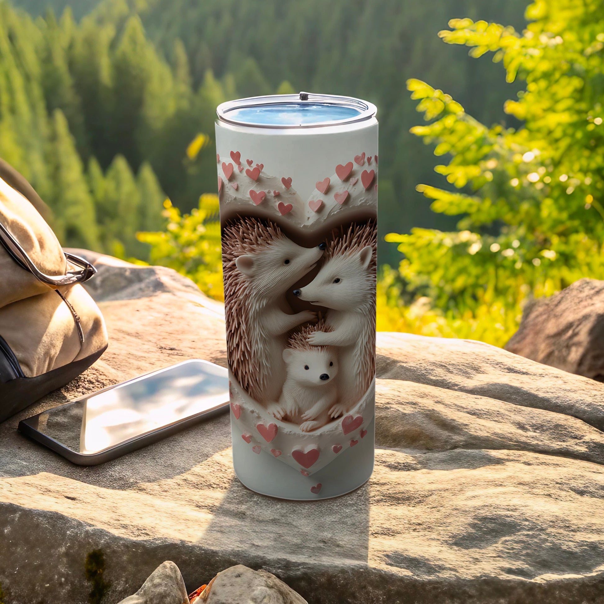 Hedgehog family inside hearts on a white tumbler, outdoors with phone and bag.