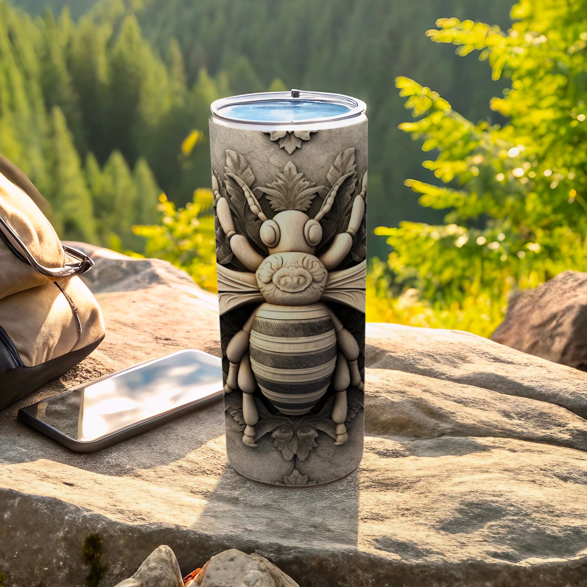 Grey textured tumbler with carved bee design on a rocky outdoor surface.