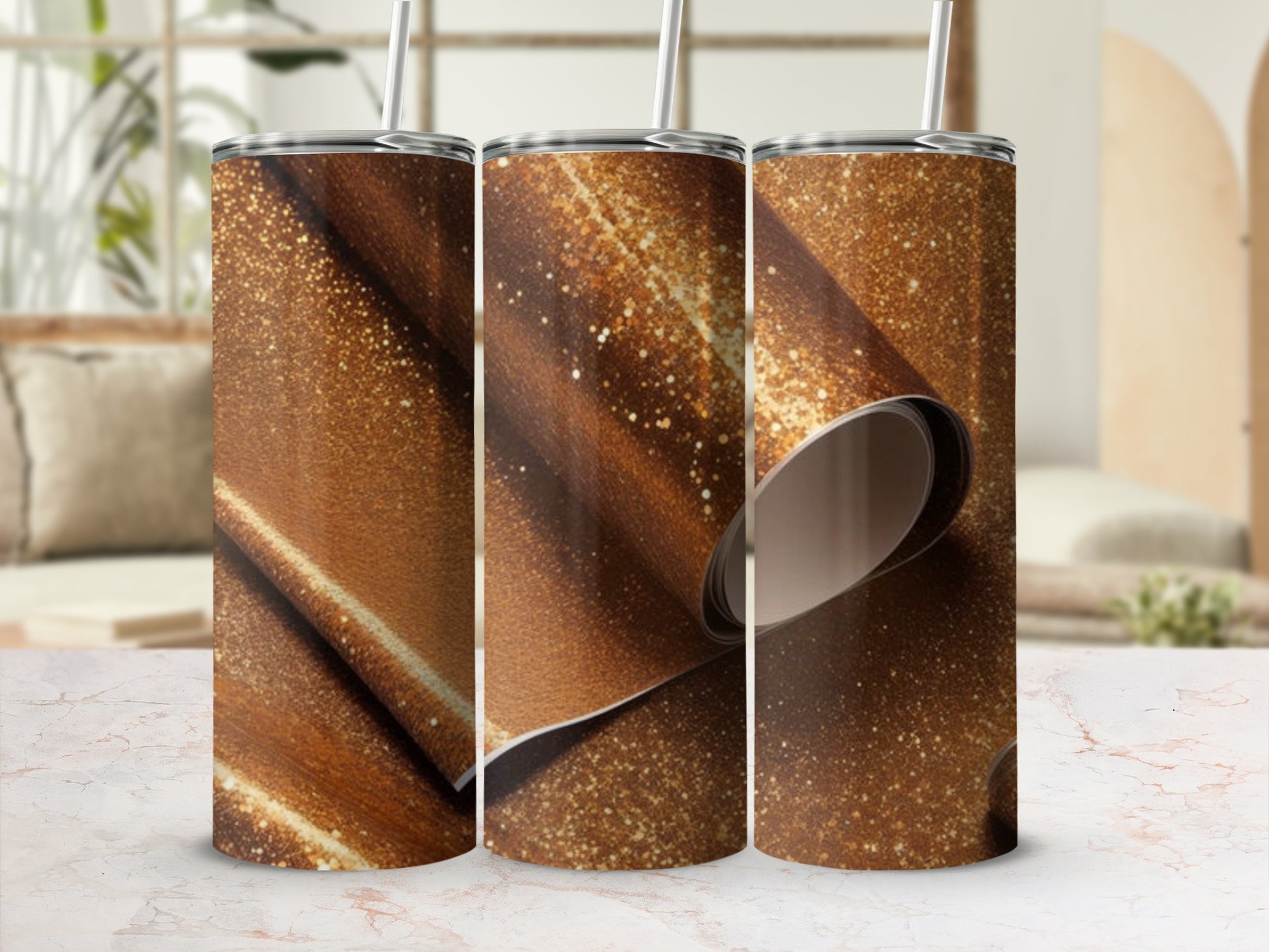 Three sparkly gold tumblers with straws on a marble surface.
