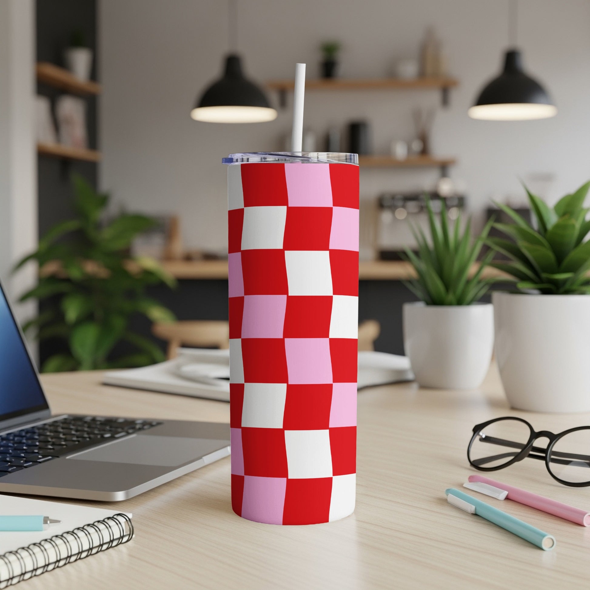 Red and pink checkered tumbler with straw on a desk.