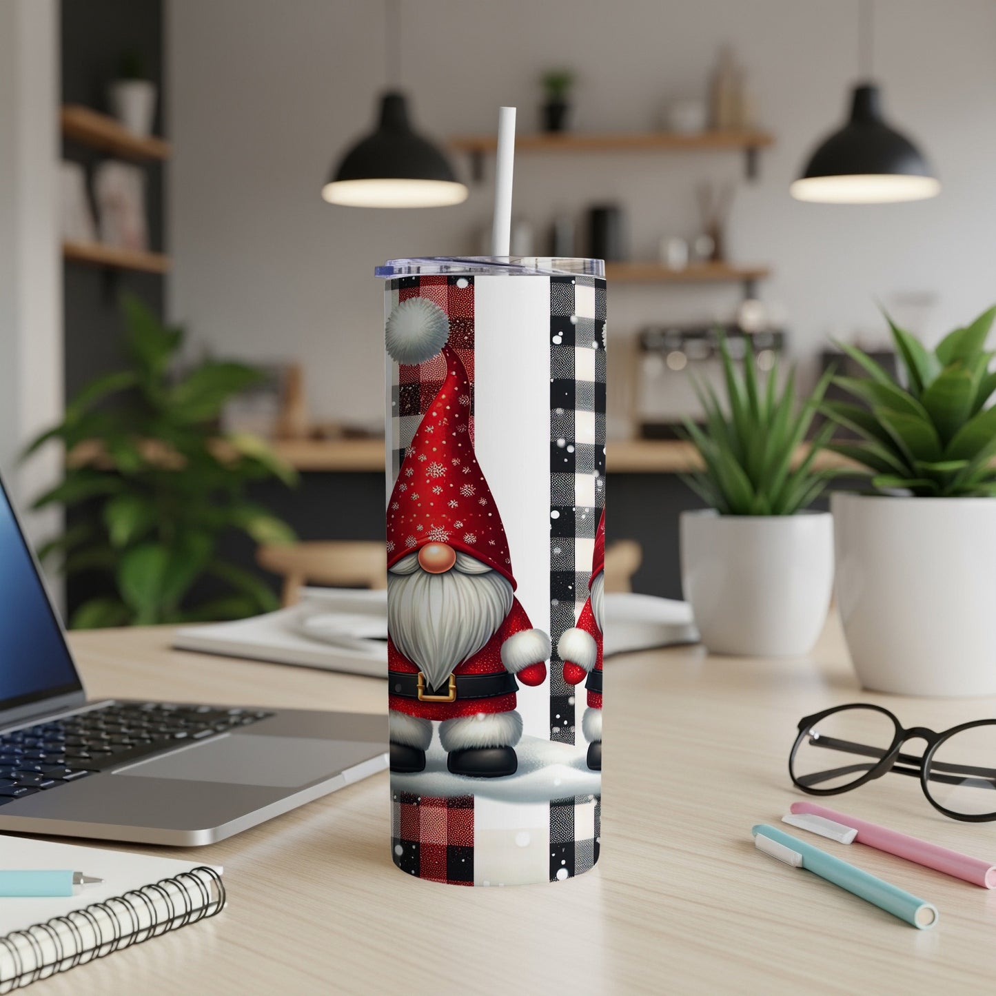 Christmas gnome on tumbler with plaid background, laptop, and plants.
