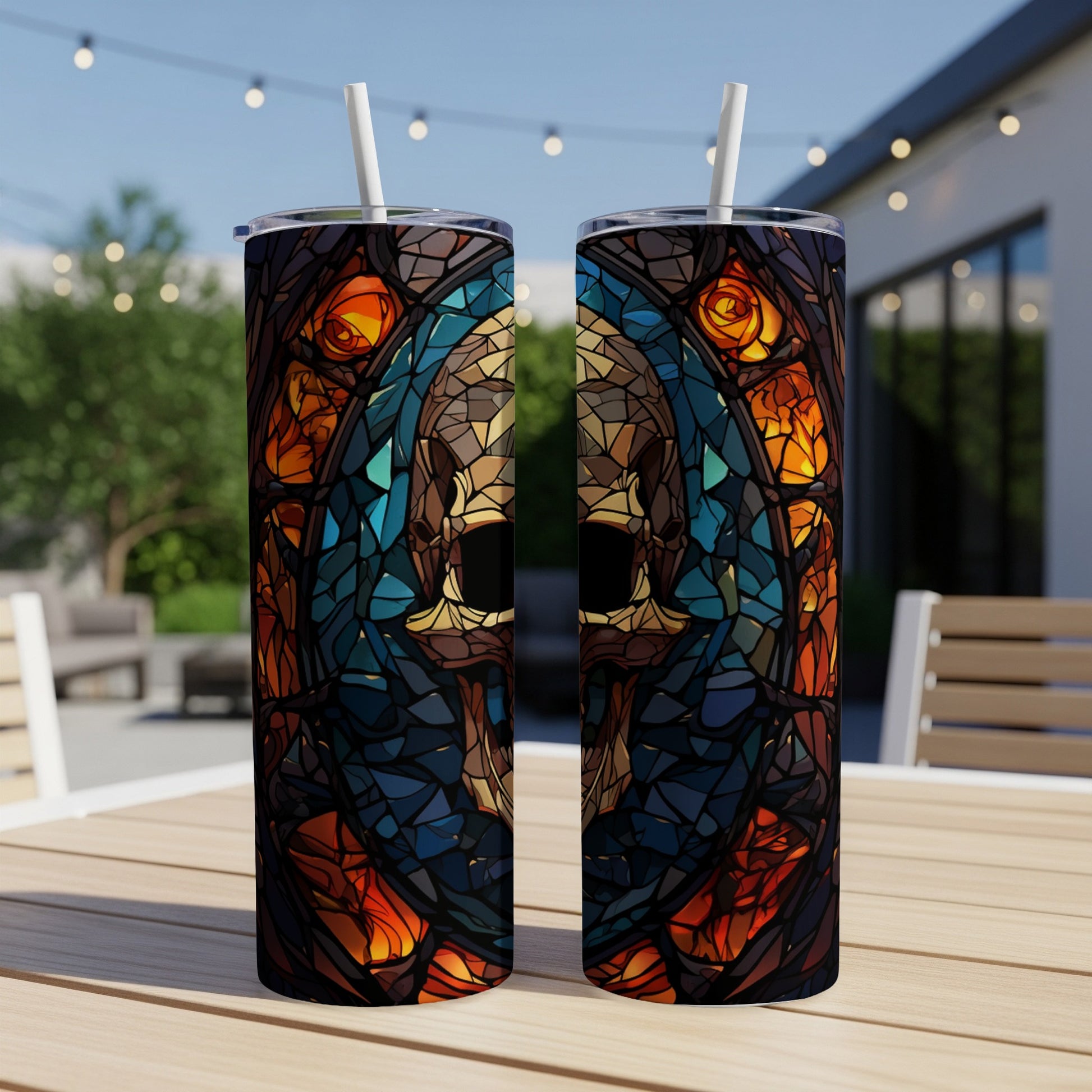 Two tumblers with stained glass skull and rose design on outdoor table.