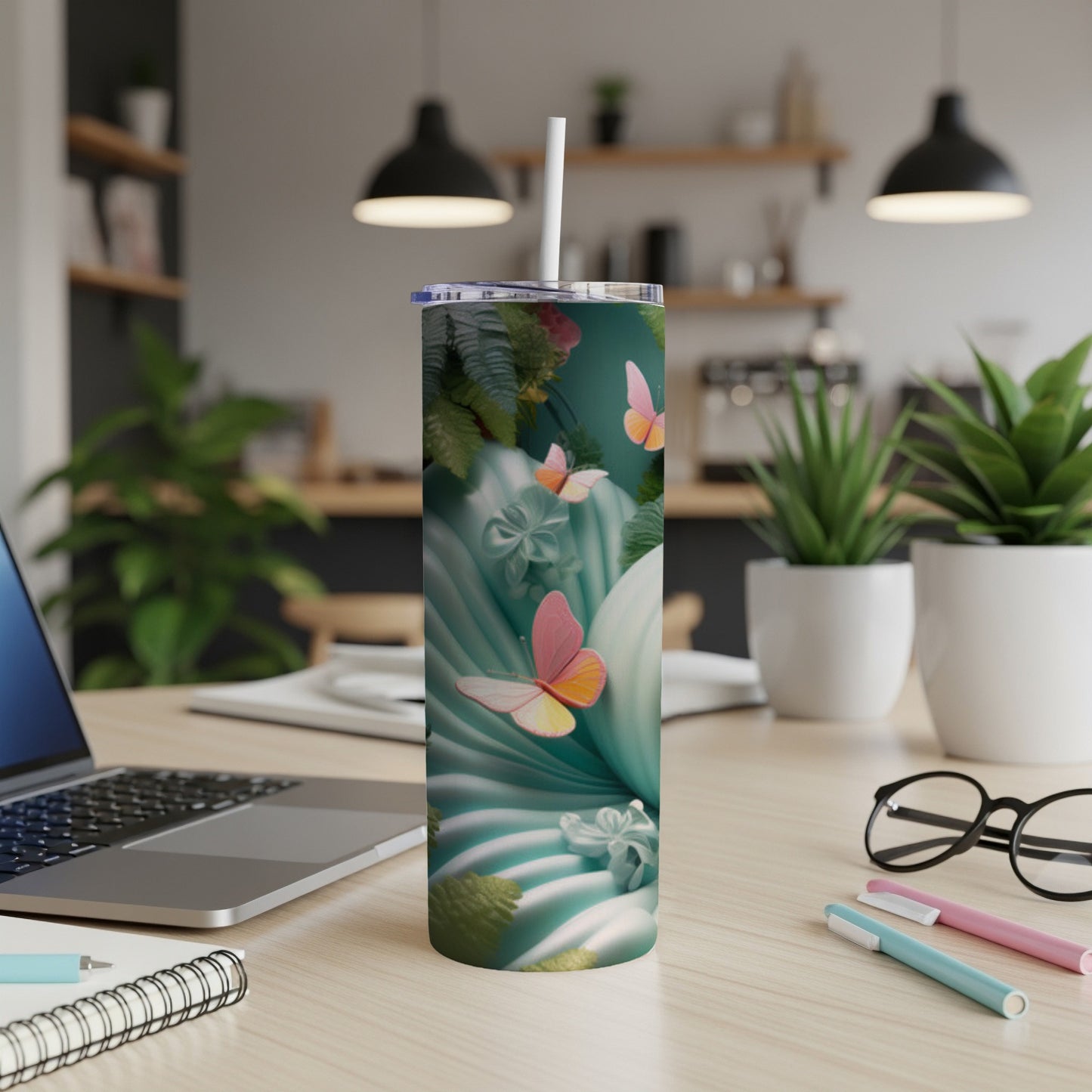 Teal tumbler with butterflies and tropical leaves, on a desk.