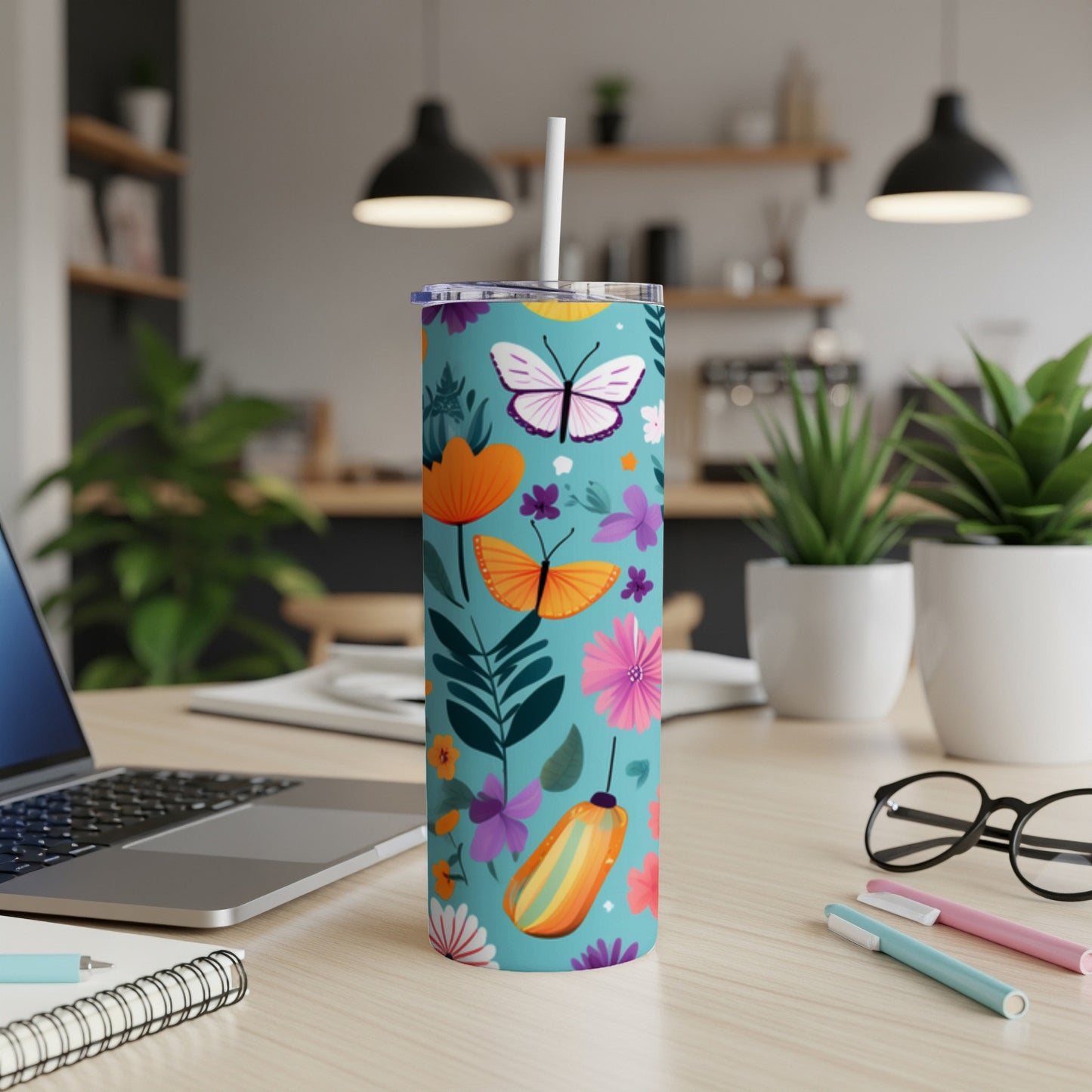 Teal tumbler with butterflies and floral pattern, with laptop and pens.