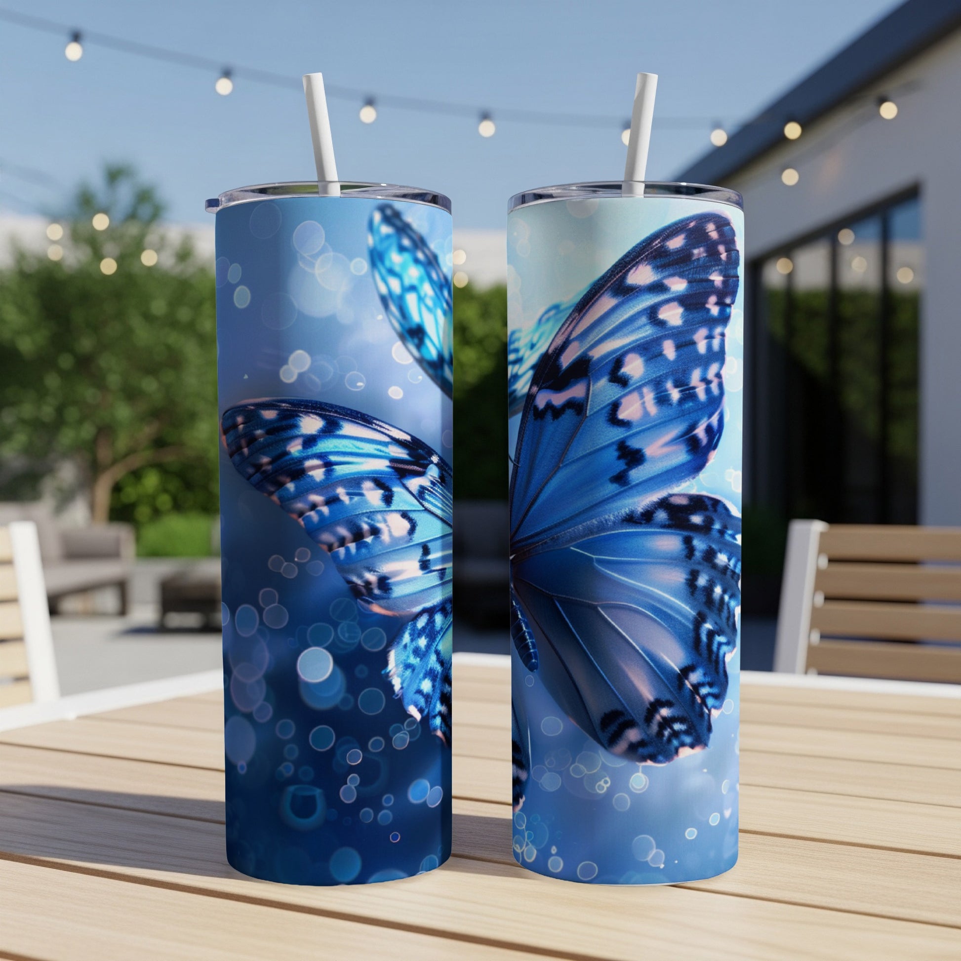 Two blue butterfly tumblers with straws on a table outdoors.