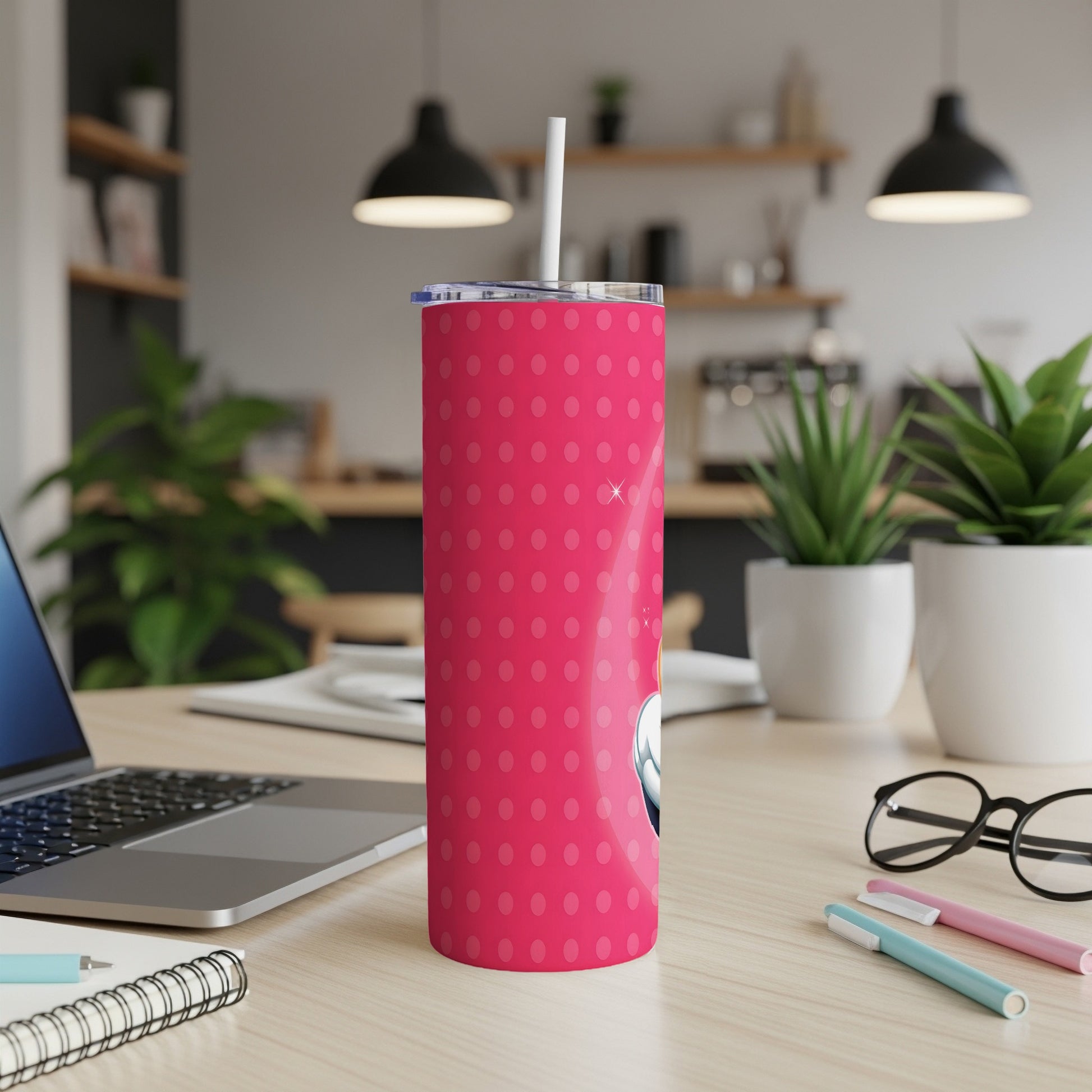Pink tumbler with white polka dots, straw, on a desk.