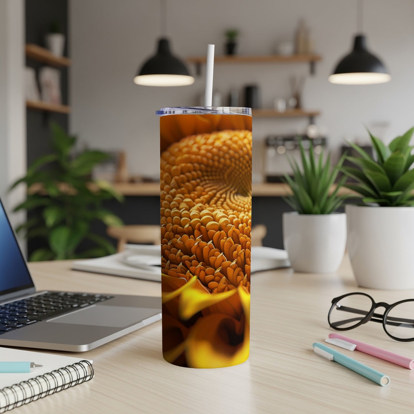 Orange textured tumbler with straw on a desk with laptop and pens.
