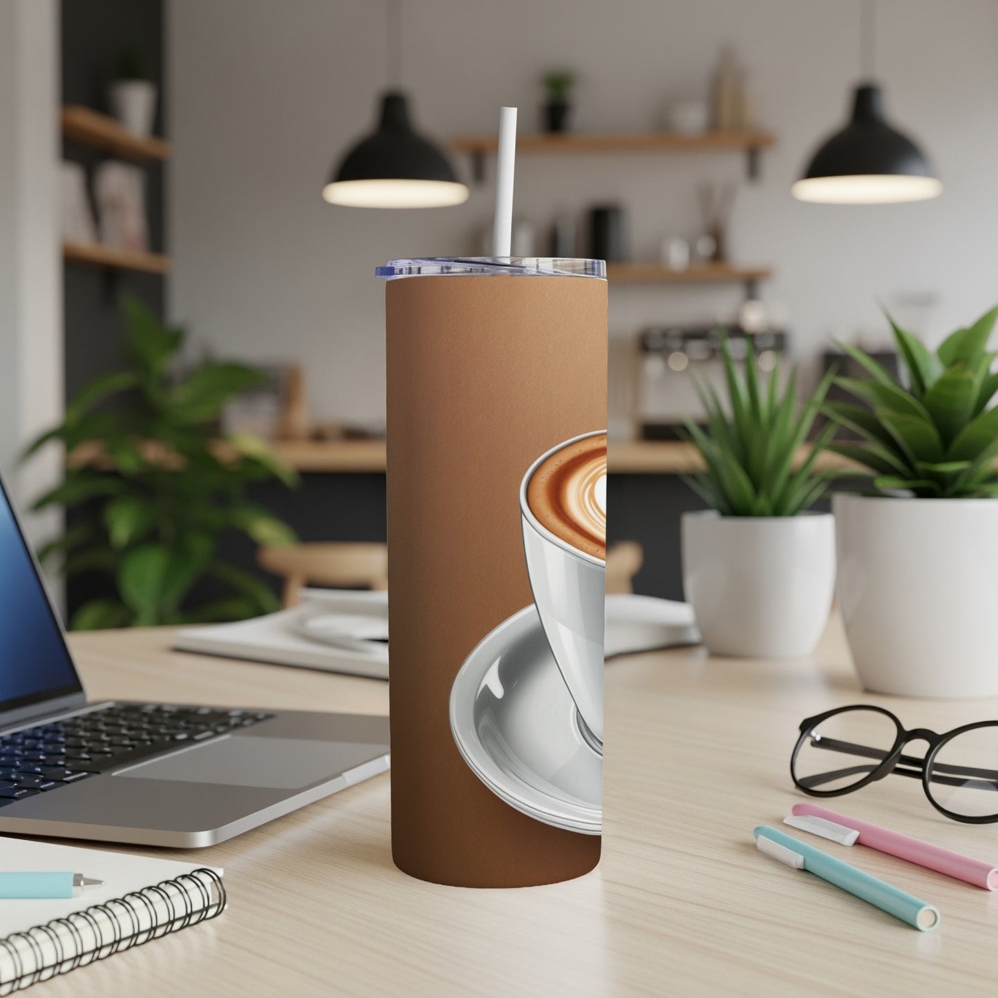 Brown tumbler with white latte art coffee cup and straw on desk.