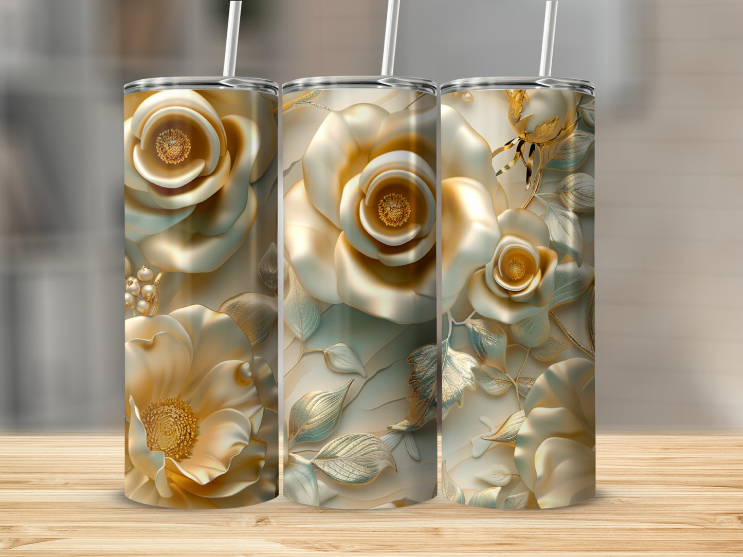 Three gold floral tumblers with straws on a wooden surface.