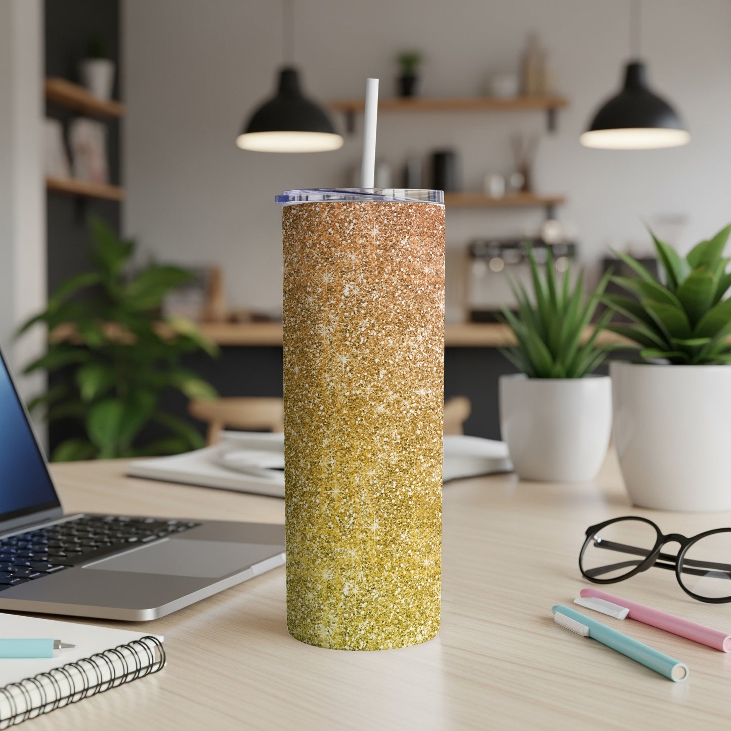 Glitter ombre tumbler with straw on a wooden desk next to a laptop.