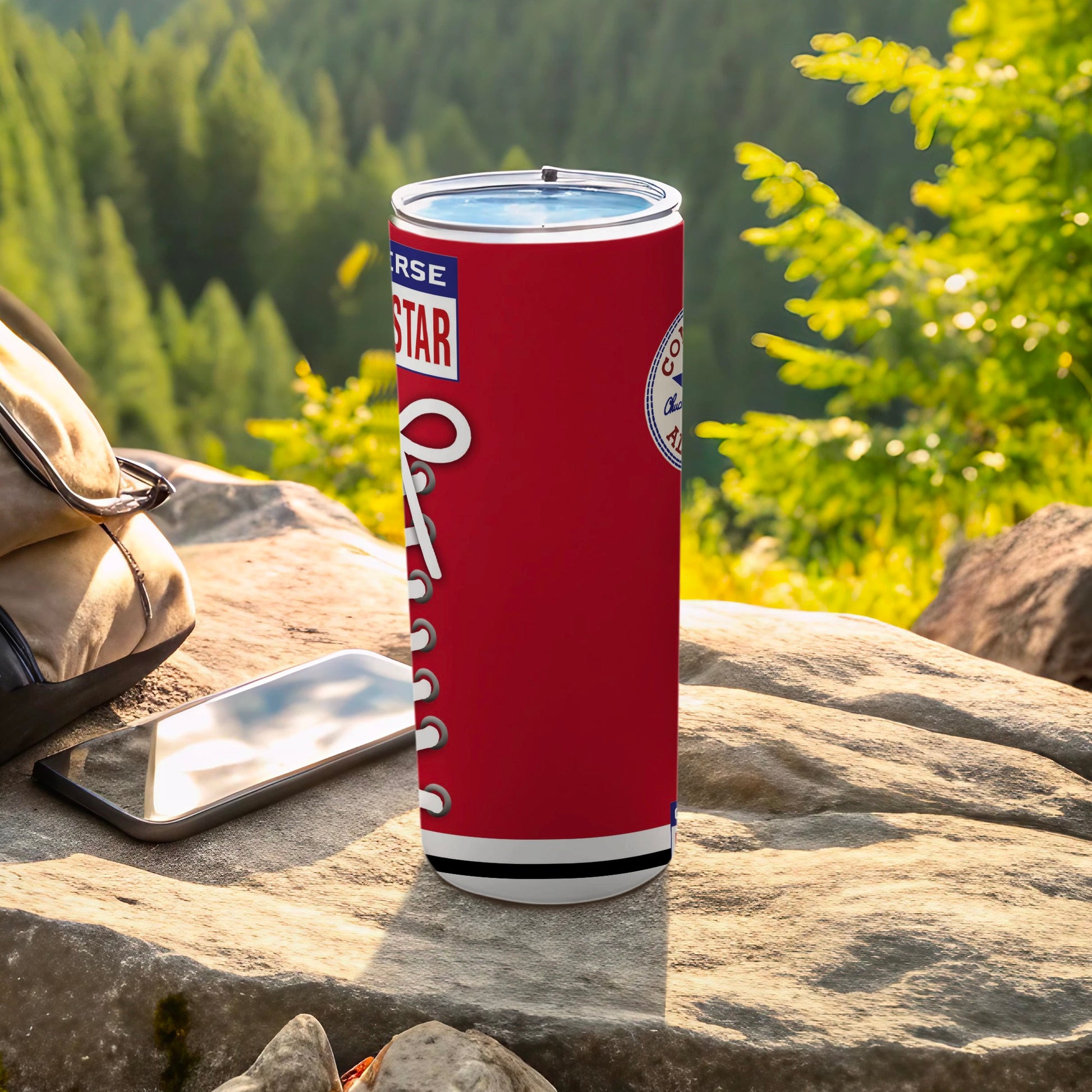 Red Converse tumbler with white laces on a rock with phone and bag.