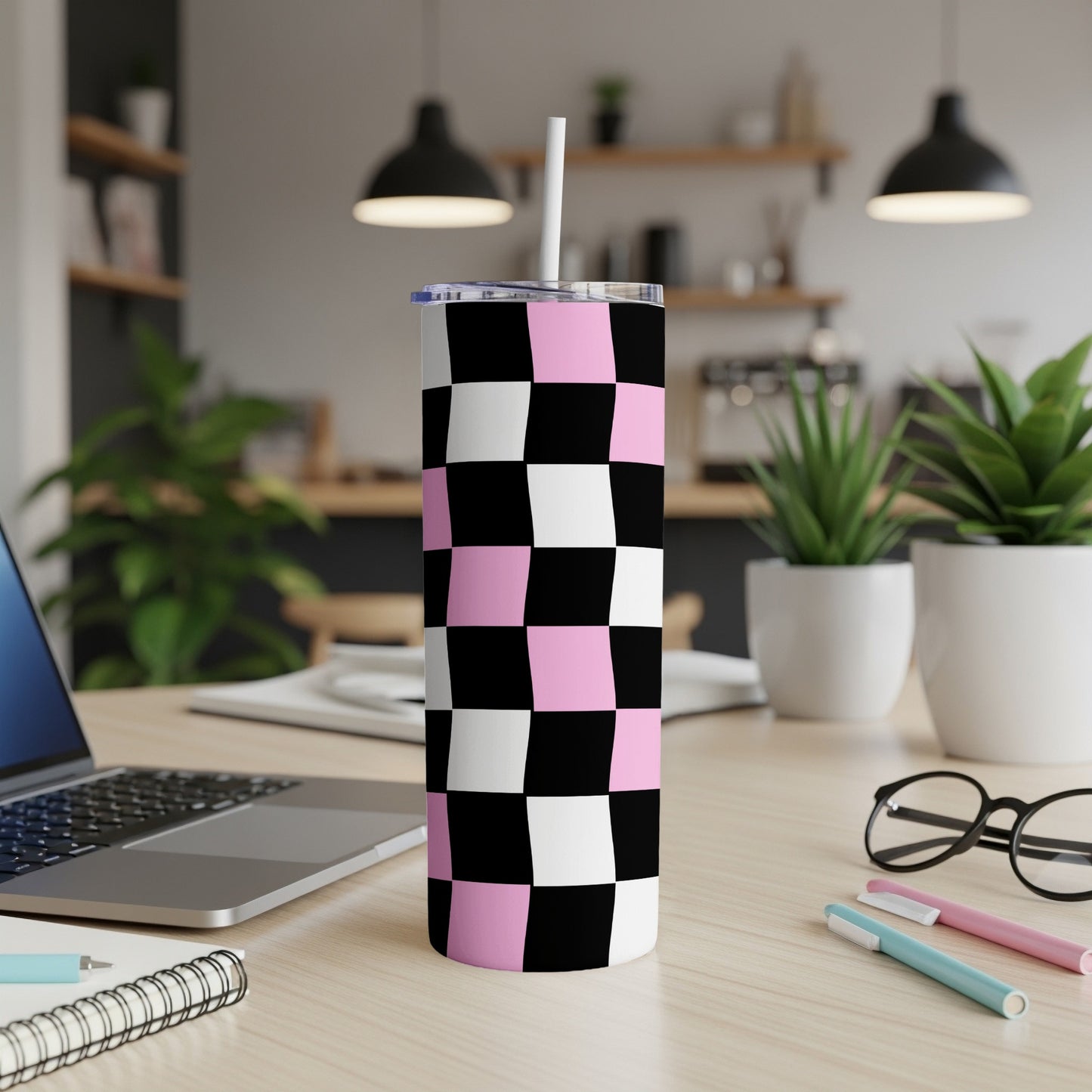 Pink and black checkerboard tumbler with straw on a desk.