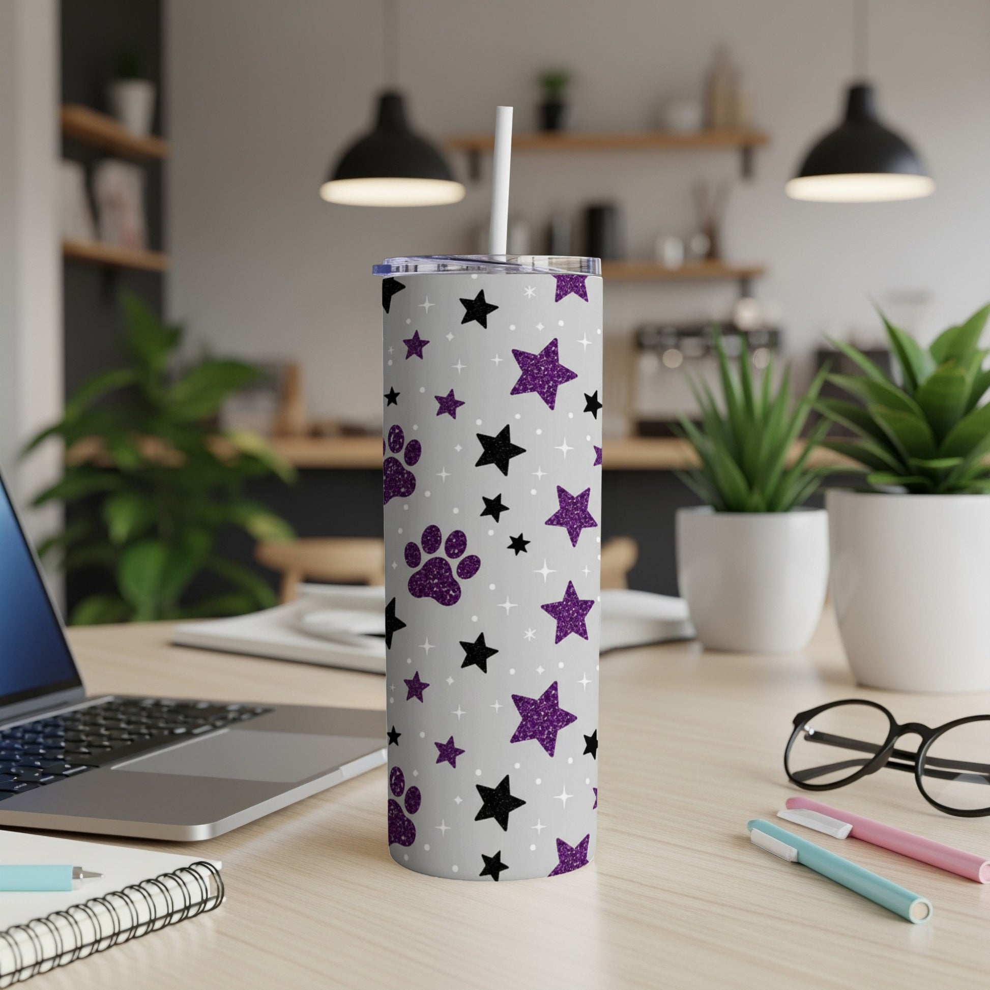Grey tumbler with purple paw prints and black glitter stars, on a desk.