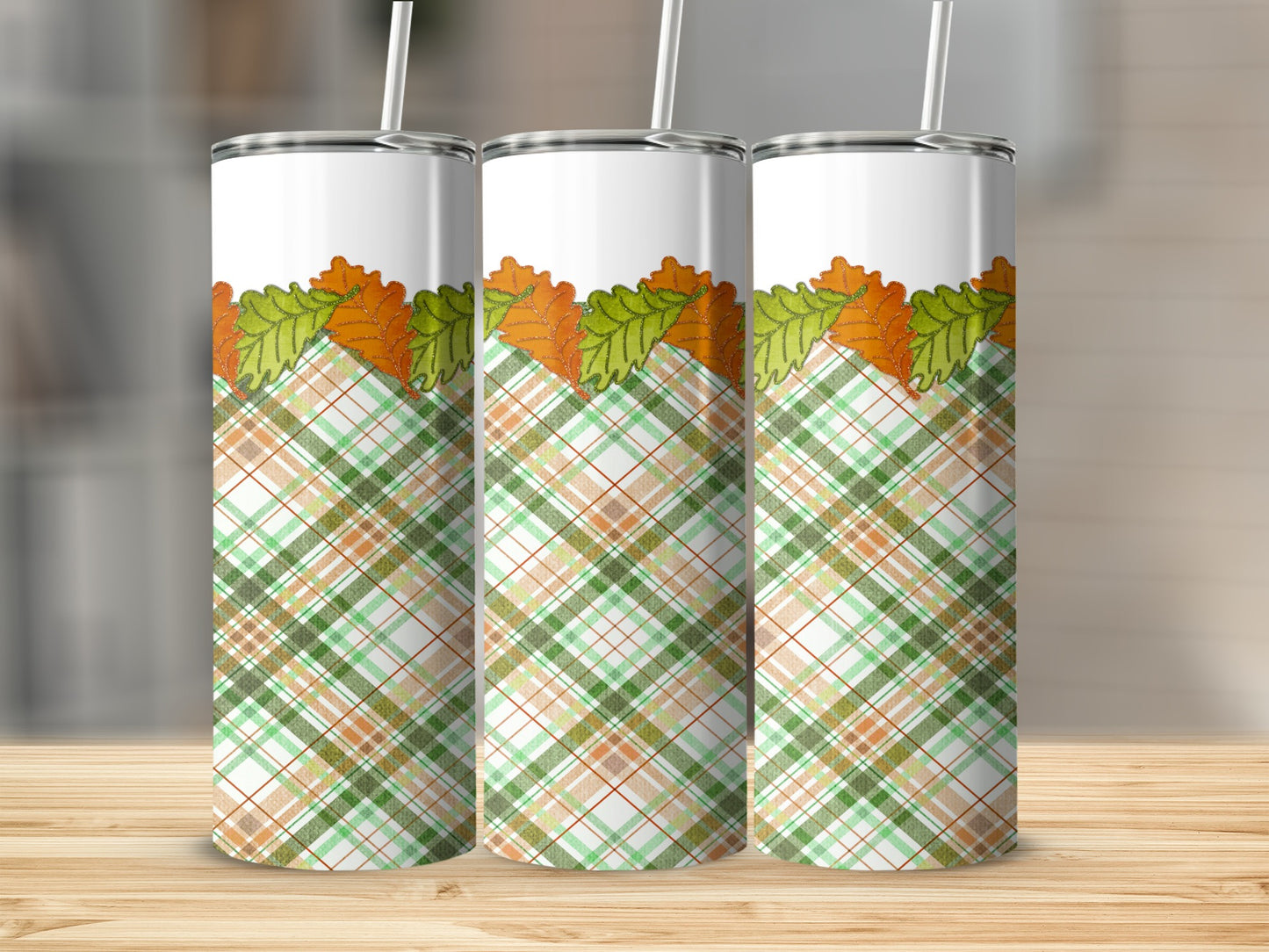 Three tumblers with plaid and autumn leaf designs on a wooden surface.