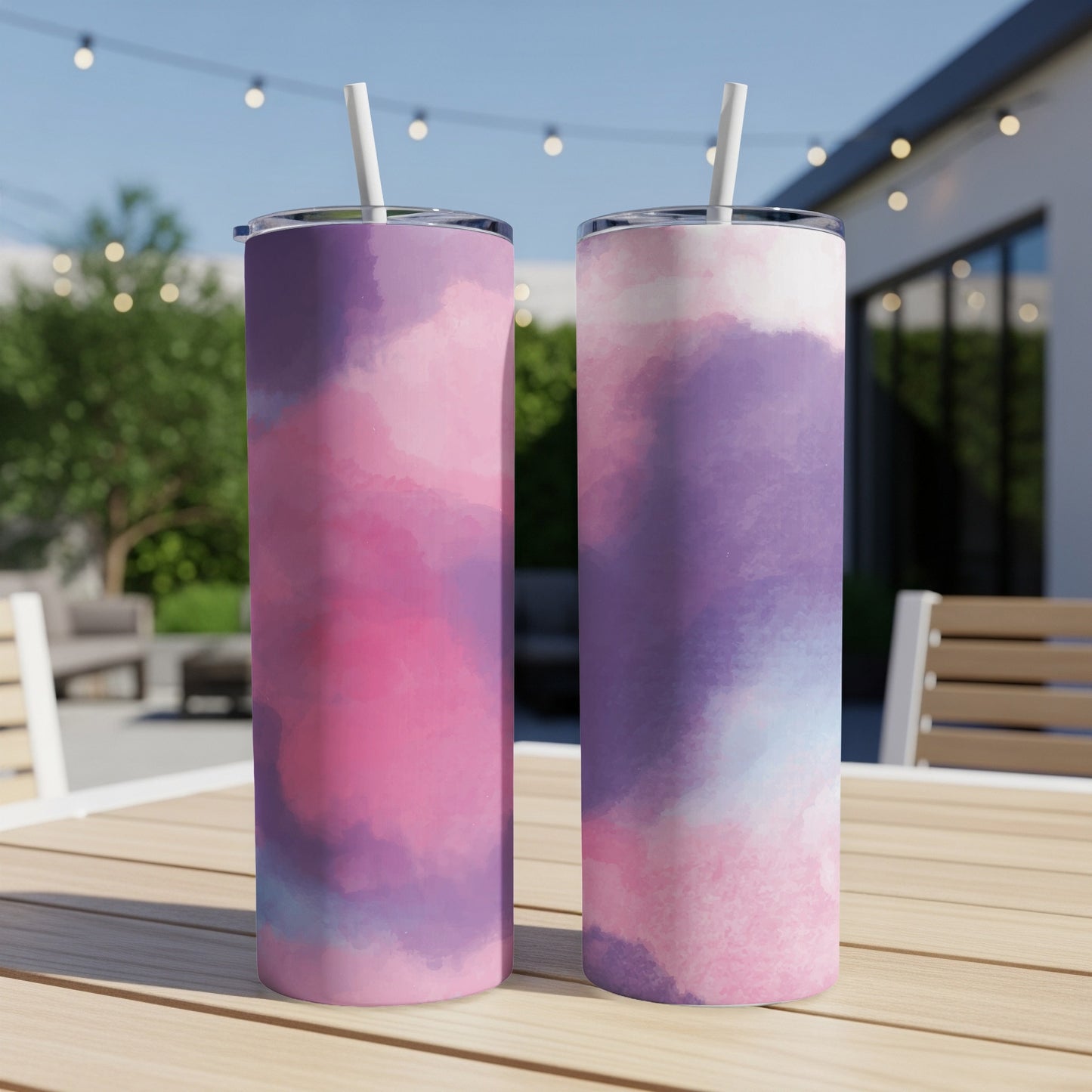 Two tumblers with pink and purple watercolor designs stand on a wooden table outdoors.