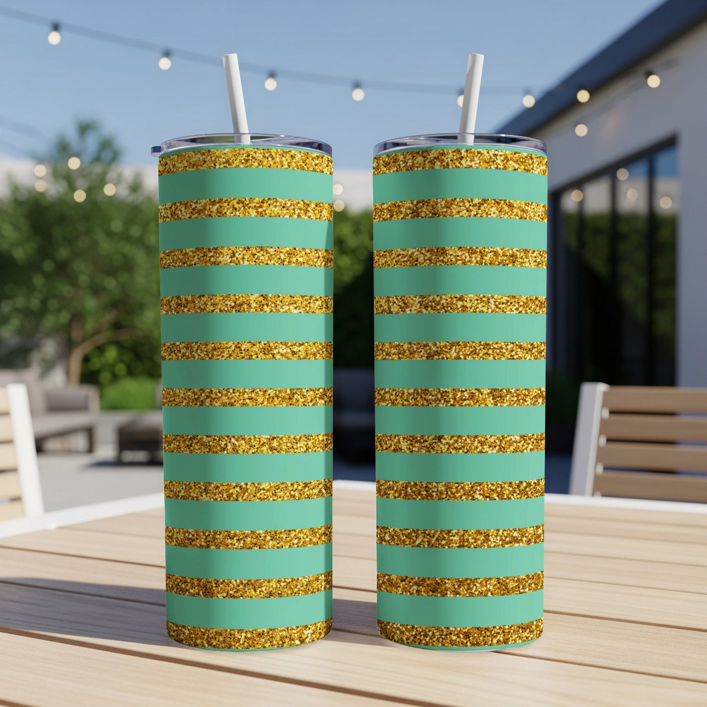 Two teal and gold glitter striped tumblers with straws on a wooden table.