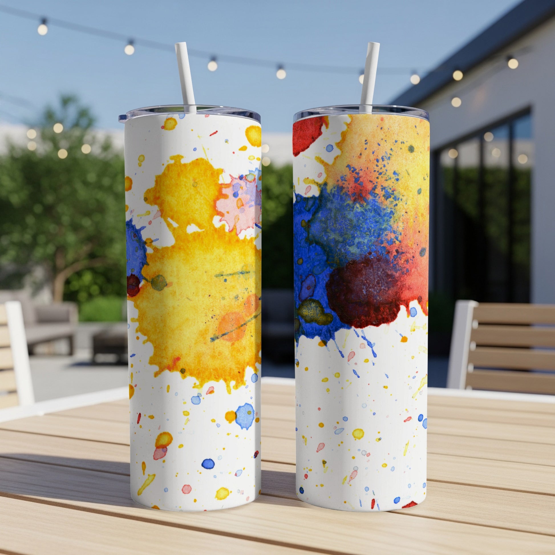 Two tumblers with colorful watercolor splashes on a wooden table.