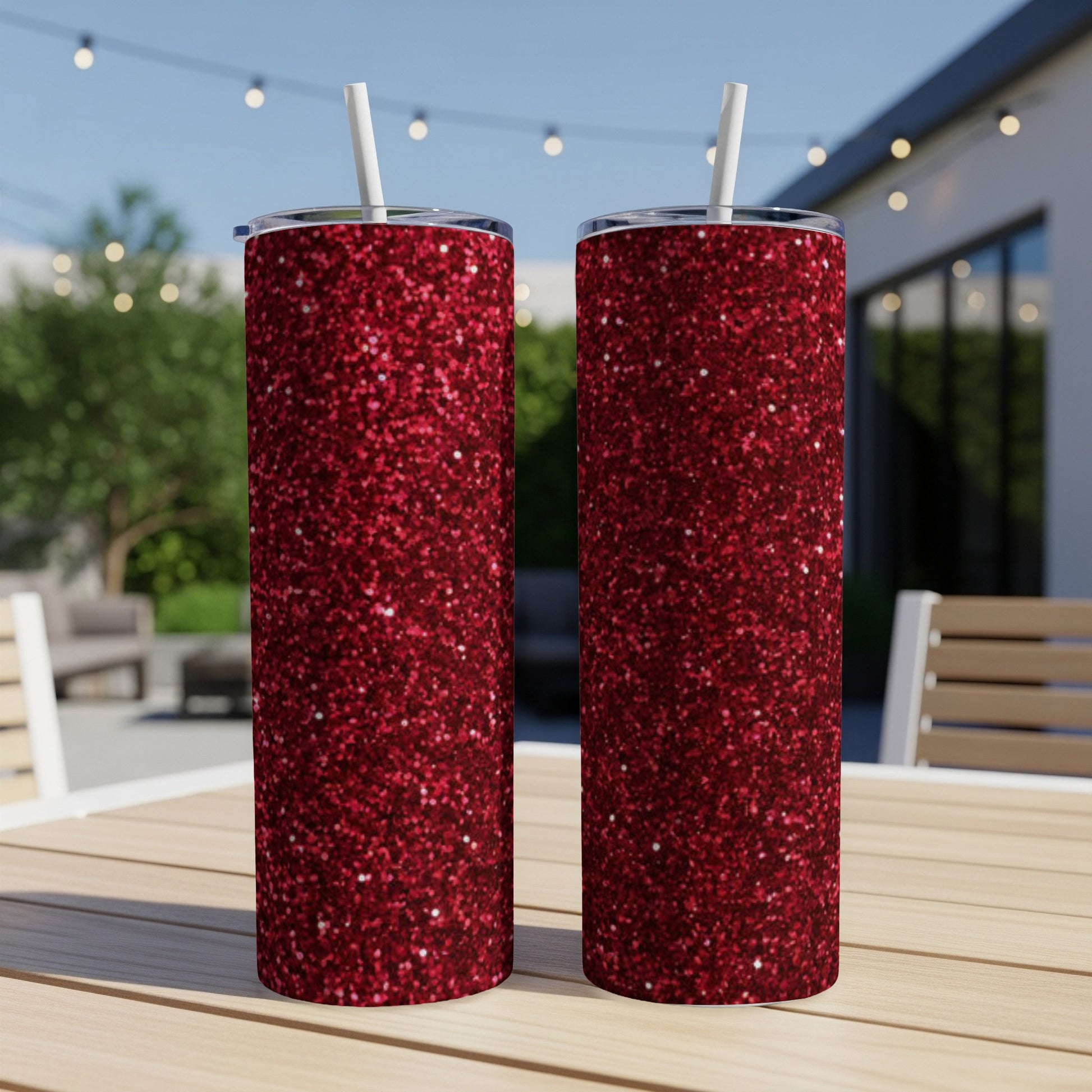 Two tall, sparkling red glitter tumblers with straws on a wooden table.